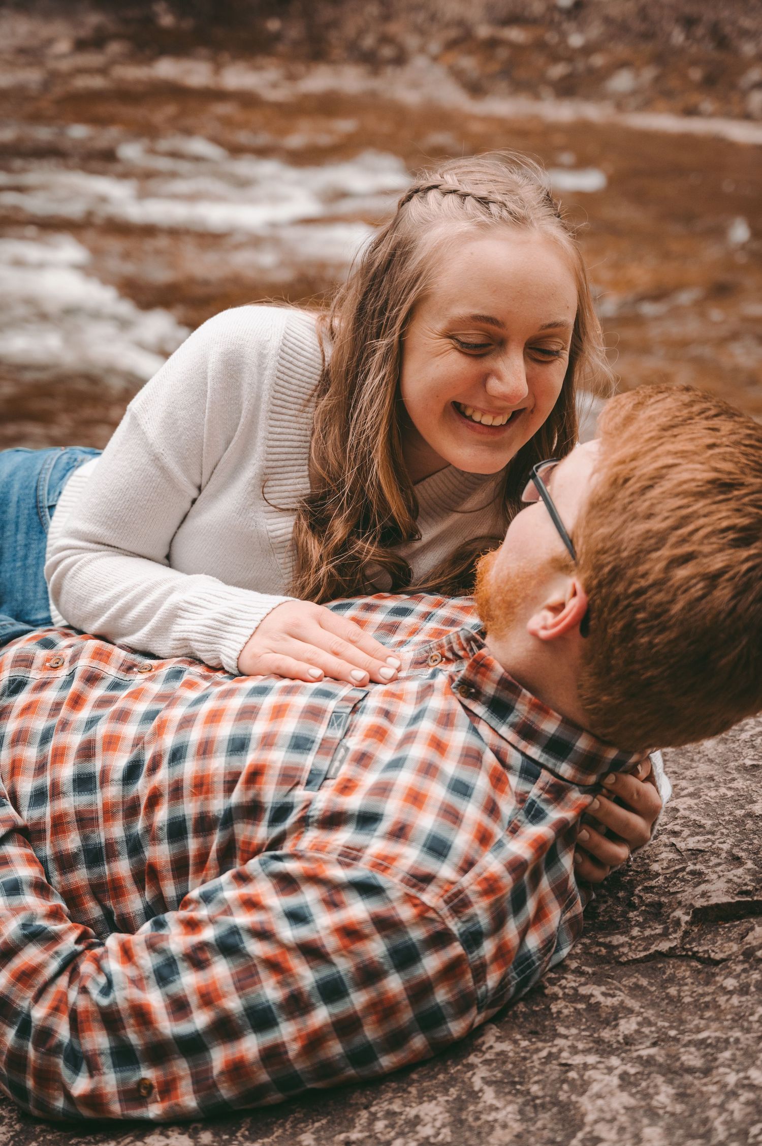 Couple lying on rock surface sharing intimate moment and laughter together.