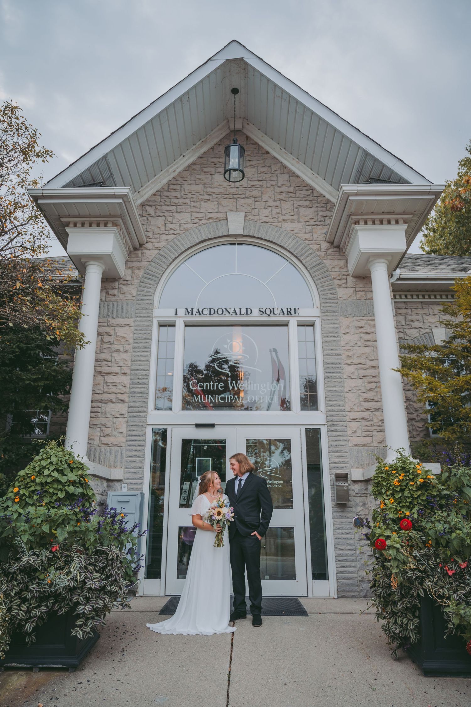 Couple poses outside MacDonald Square building entrance with stone facade and white columns.