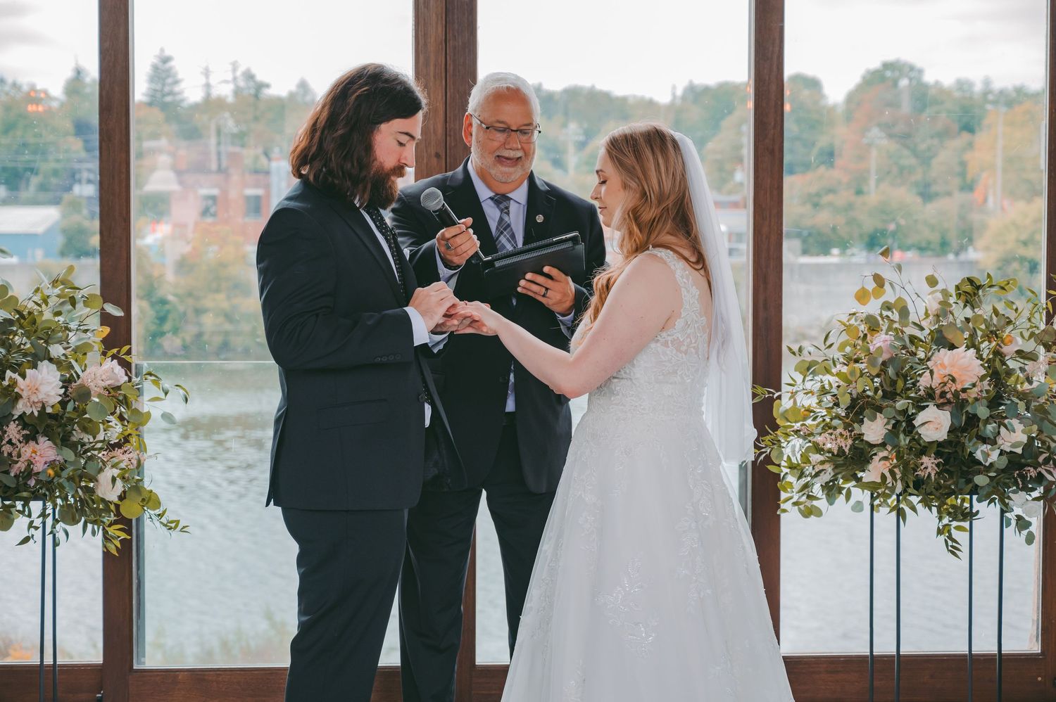 Wedding ceremony with water view through large windows and white floral arrangements.