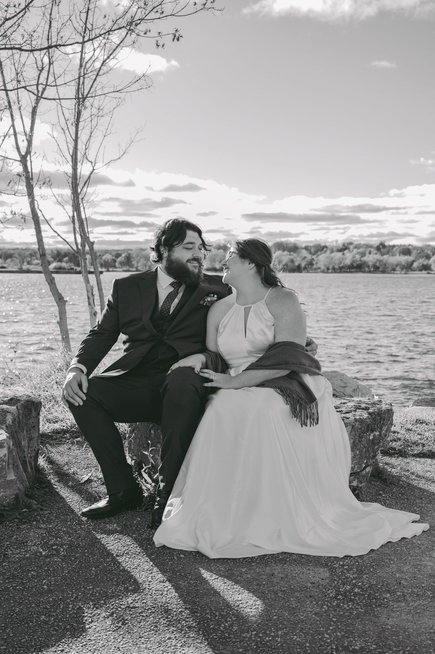 A black and white lakeside wedding portrait of a couple sharing an intimate moment while seated.