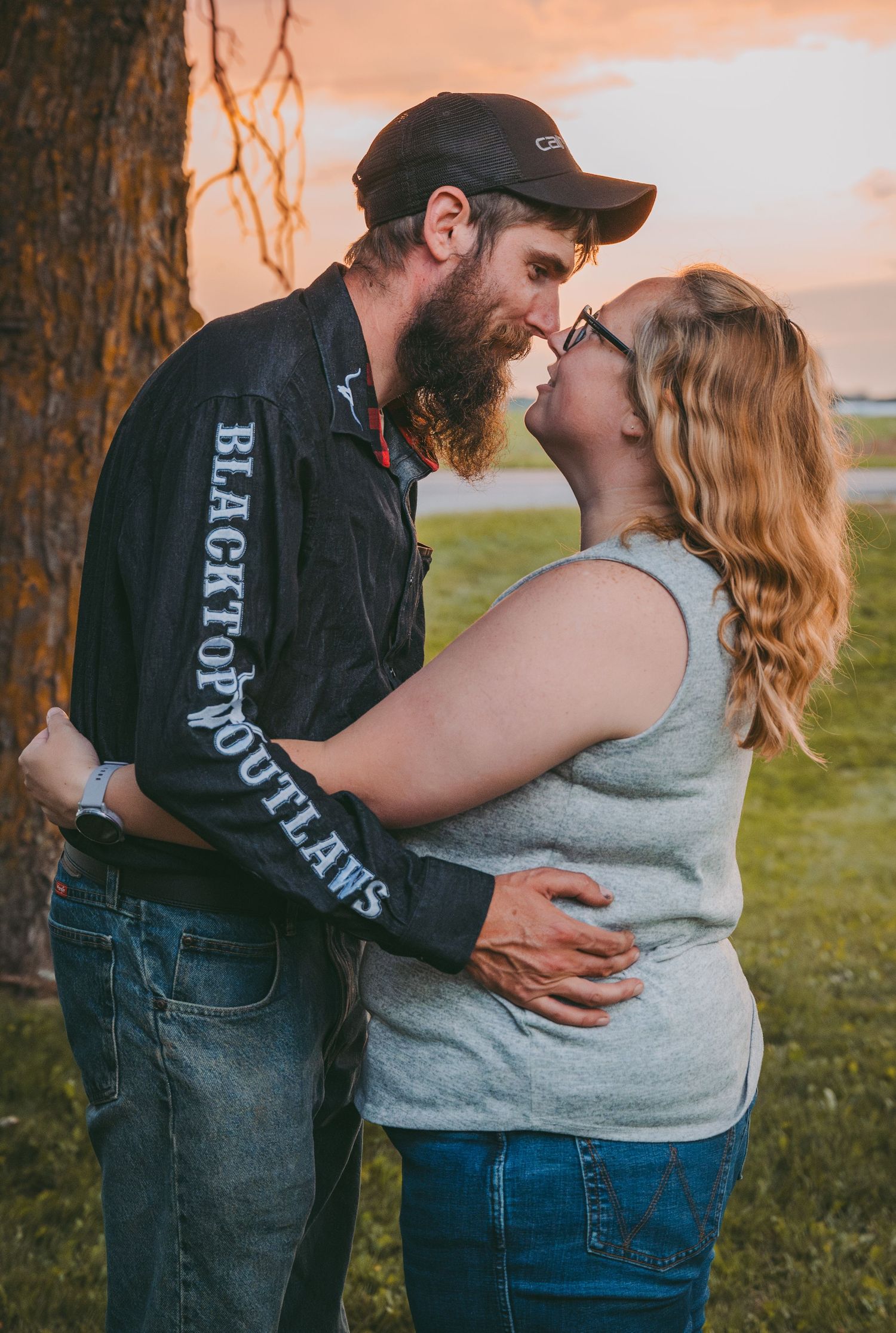A sunset embrace between a couple against a tree with orange sky in background.