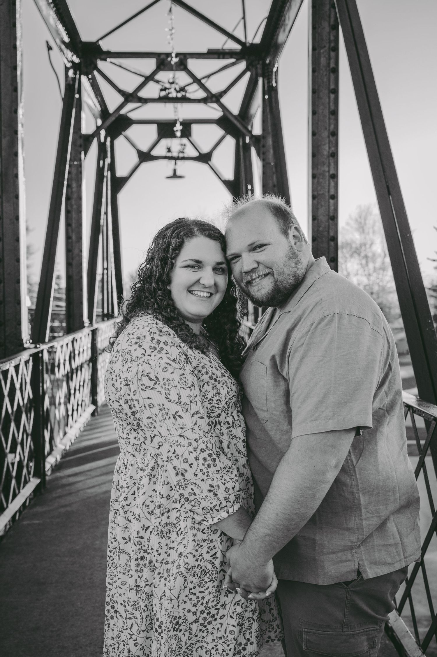 A black and white portrait of a couple in love posing on an industrial bridge structure.