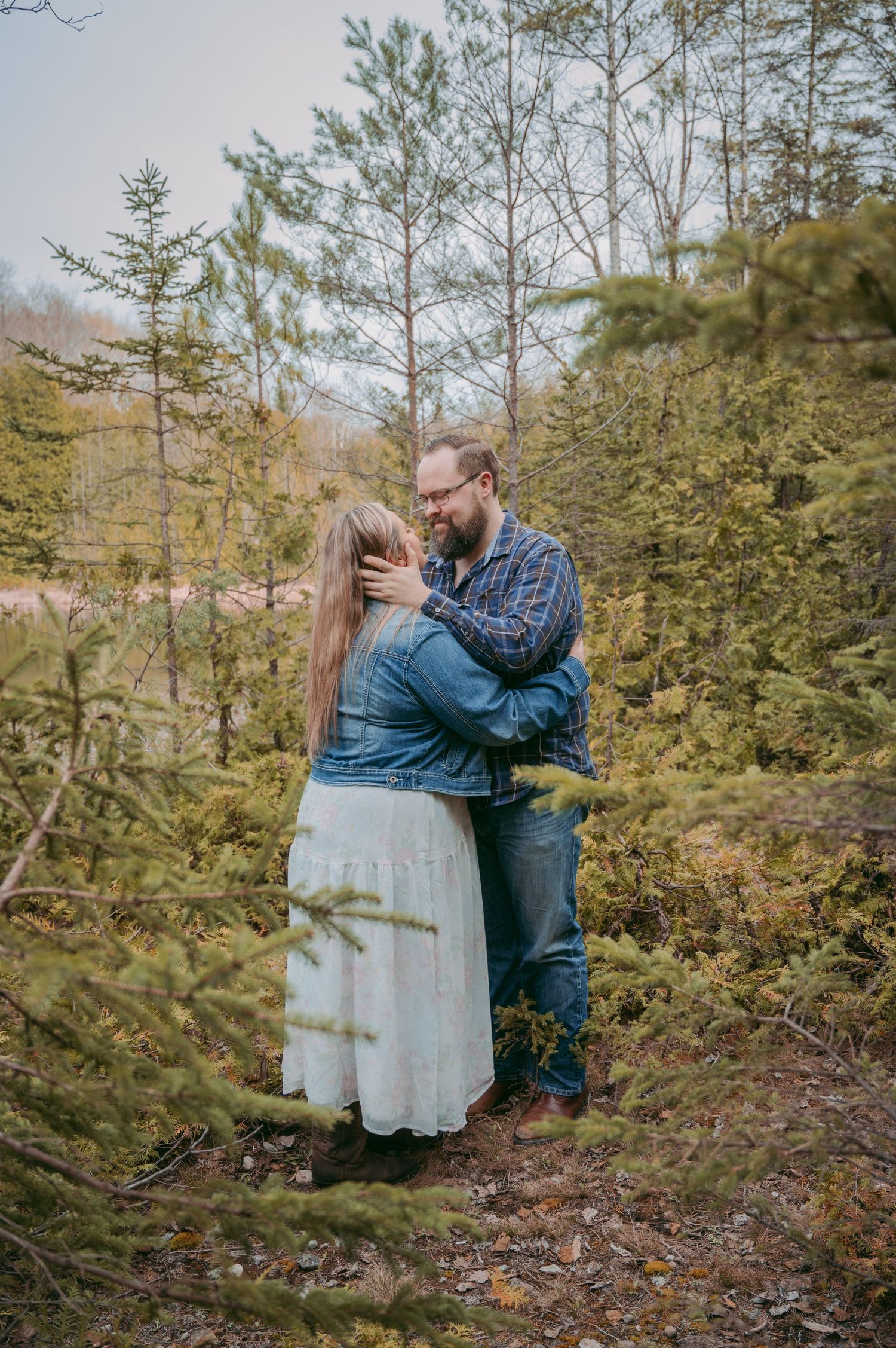Couple embracing on a hillside surrounded by evergreen trees and natural foliage.