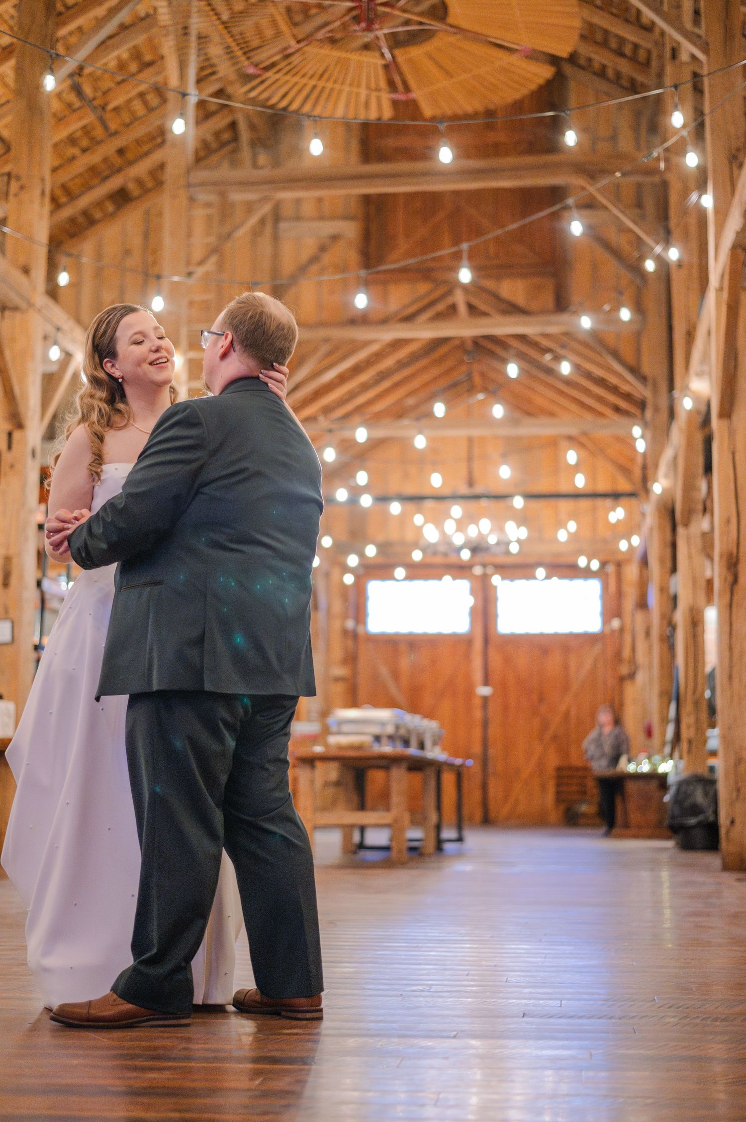 Couple shares first dance in a rustic barn wedding venue adorned with string lights and warm wood walls.