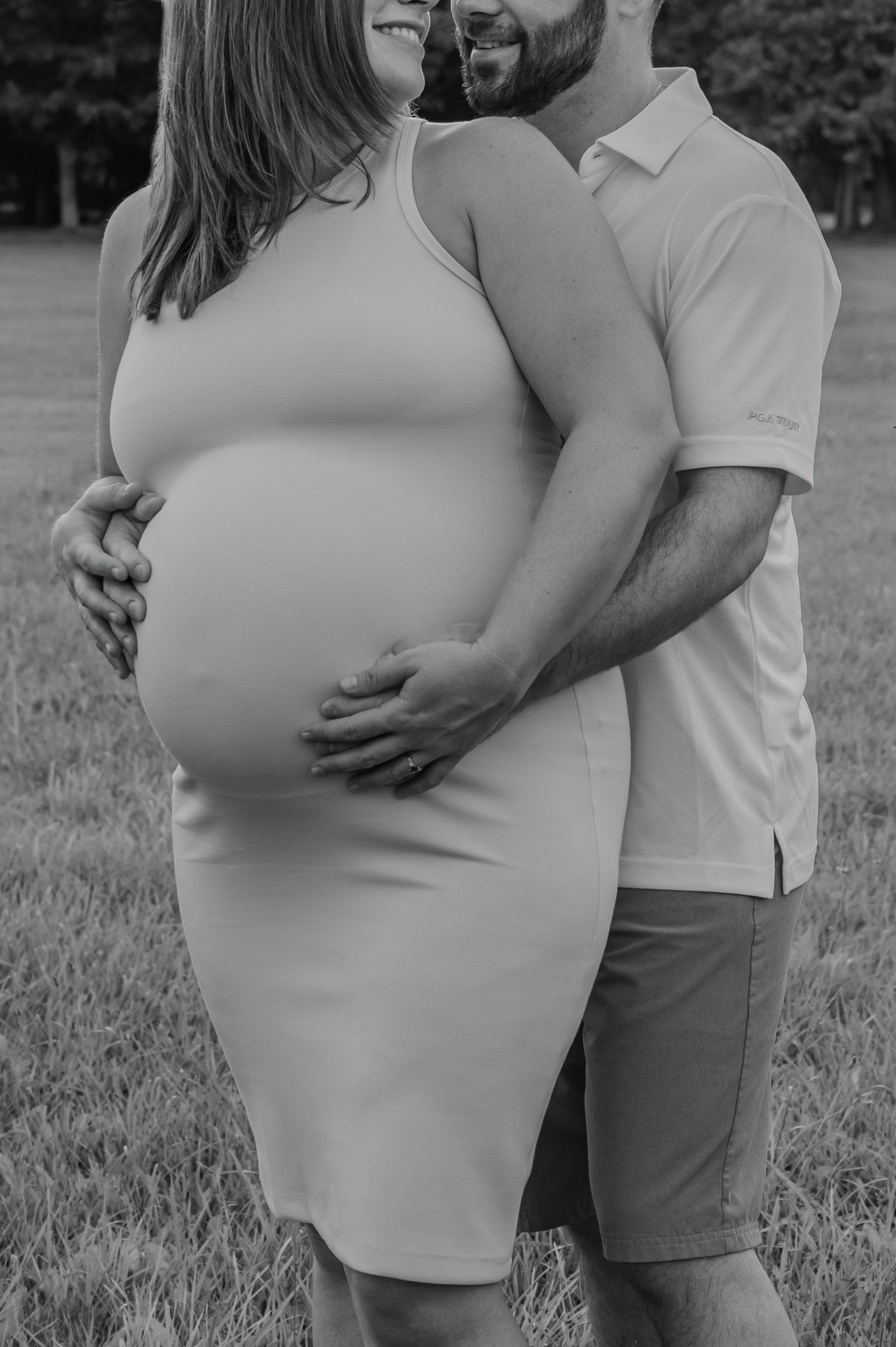 A tender moment captured in black and white as a couple embraces in a grassy outdoor setting during their maternity session.