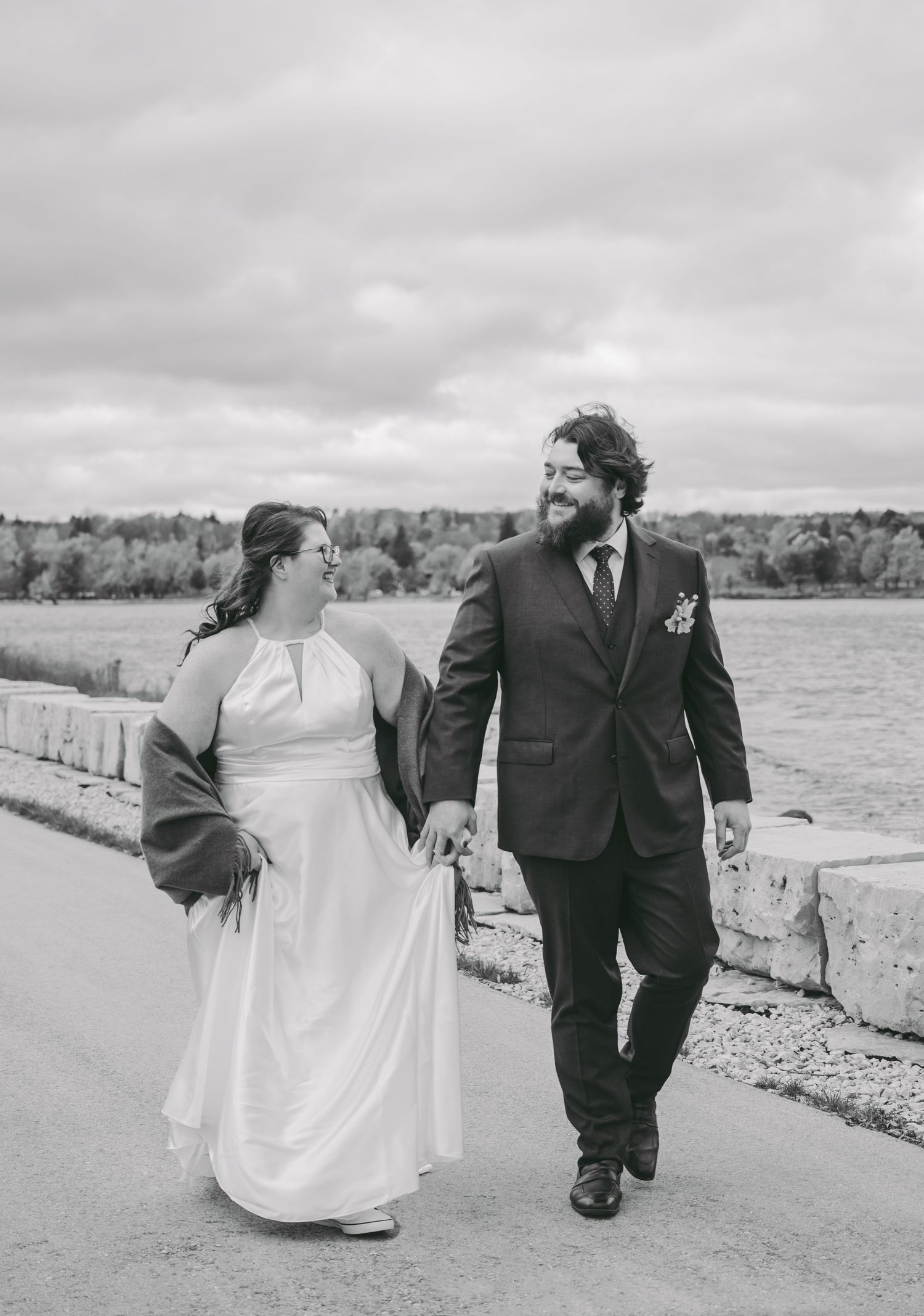 A couple walks along a rocky beach shore on their wedding day in black and white photography.