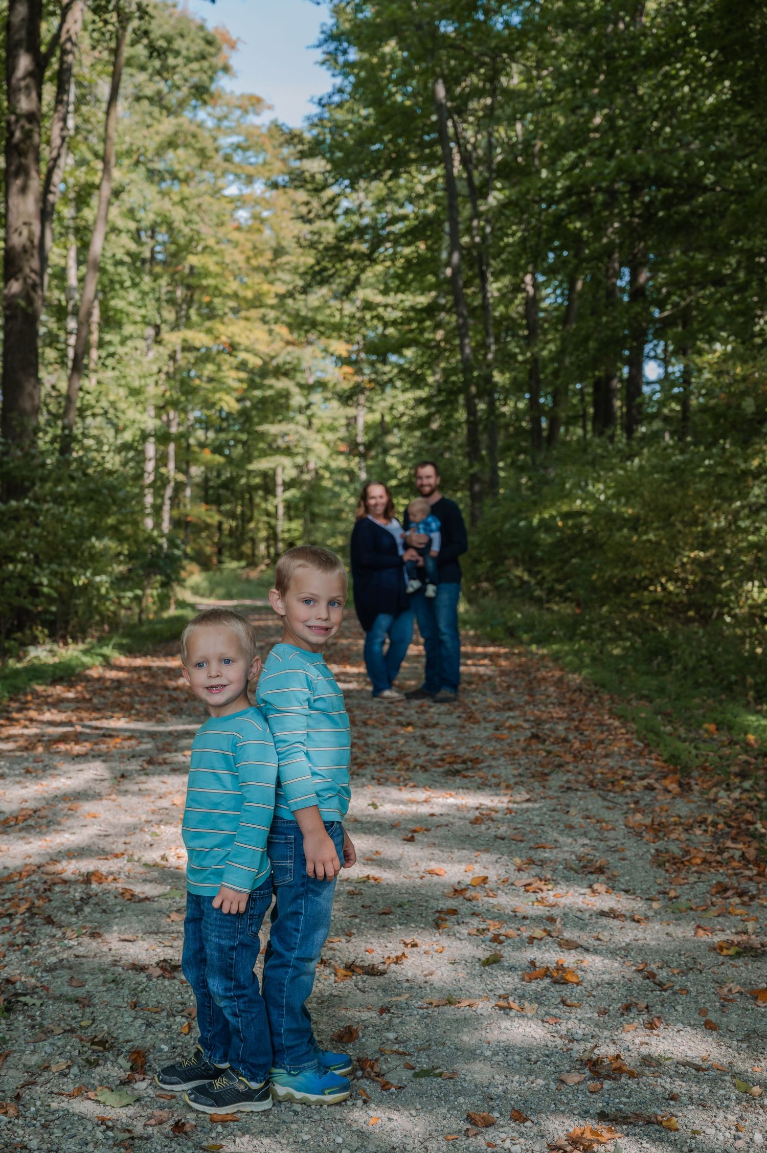 Family enjoying a walk together on a tree-lined autumn trail covered with fallen leaves.