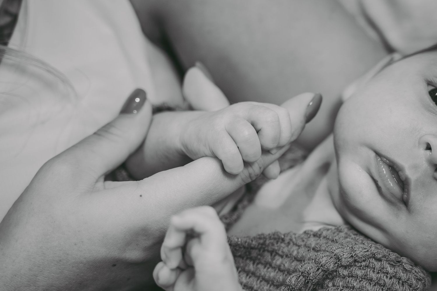 Close-up black and white shot of tiny baby hands being held.