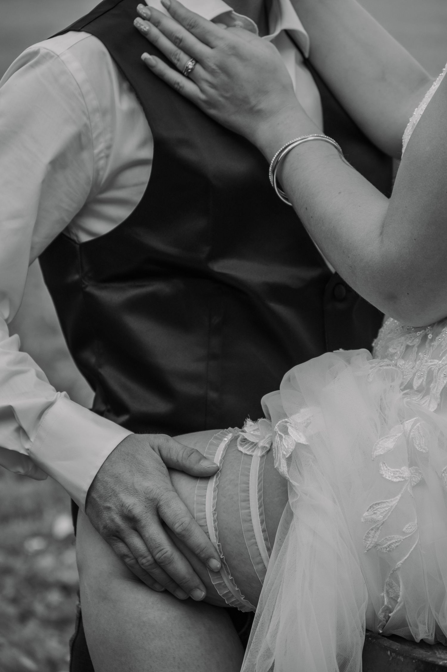 A black and white close-up photograph of hands resting on a lap with delicate lace wedding dress fabric visible.