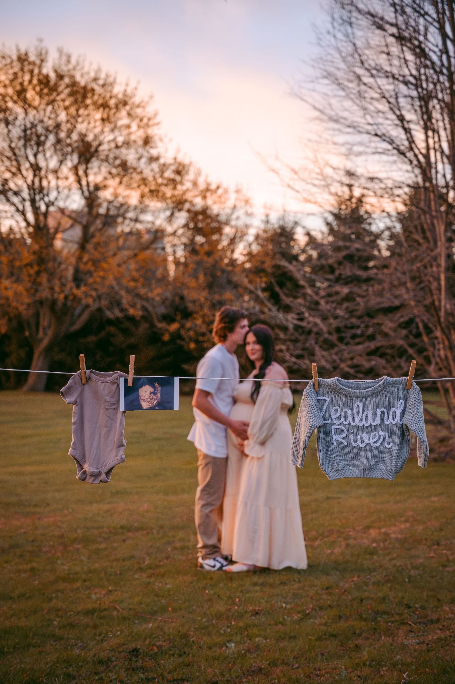 Maternity photo with baby clothes on clothesline at sunset.