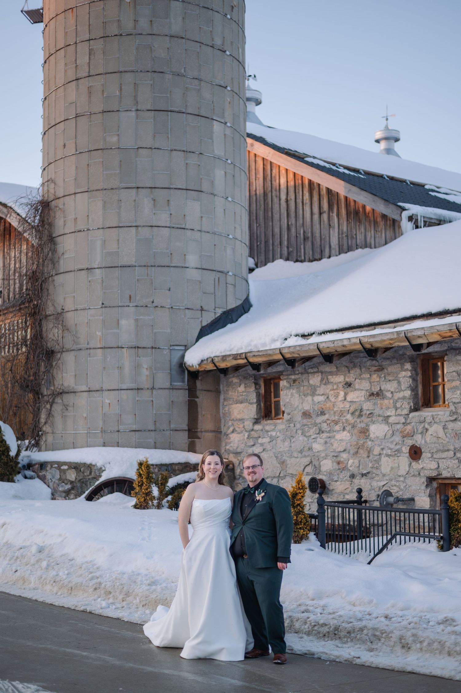 A winter wedding scene with a snowy barn and silo backdrop at the rustic Brussels Four Winds Barn.