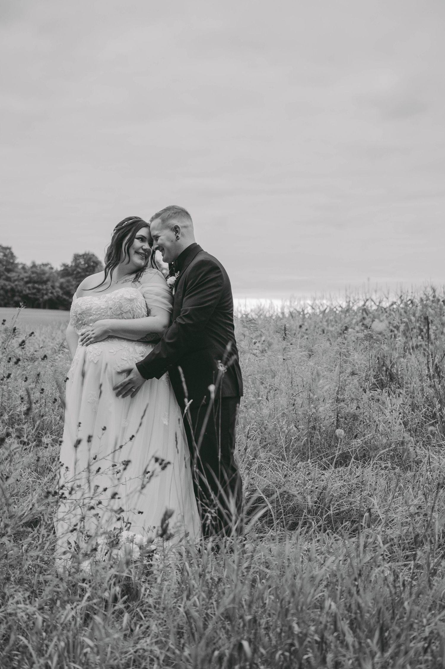 Black and white photo of a couple in wedding attire embracing in a wildflower field on their wedding day.