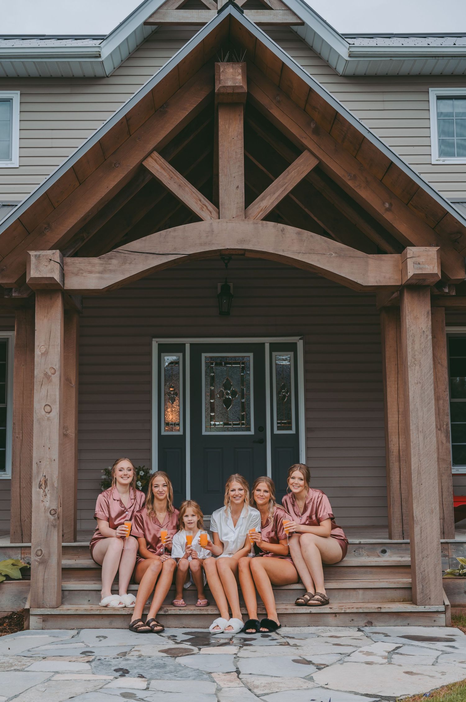 Group in matching pink outfits sitting on porch steps of house with wooden beam entrance.