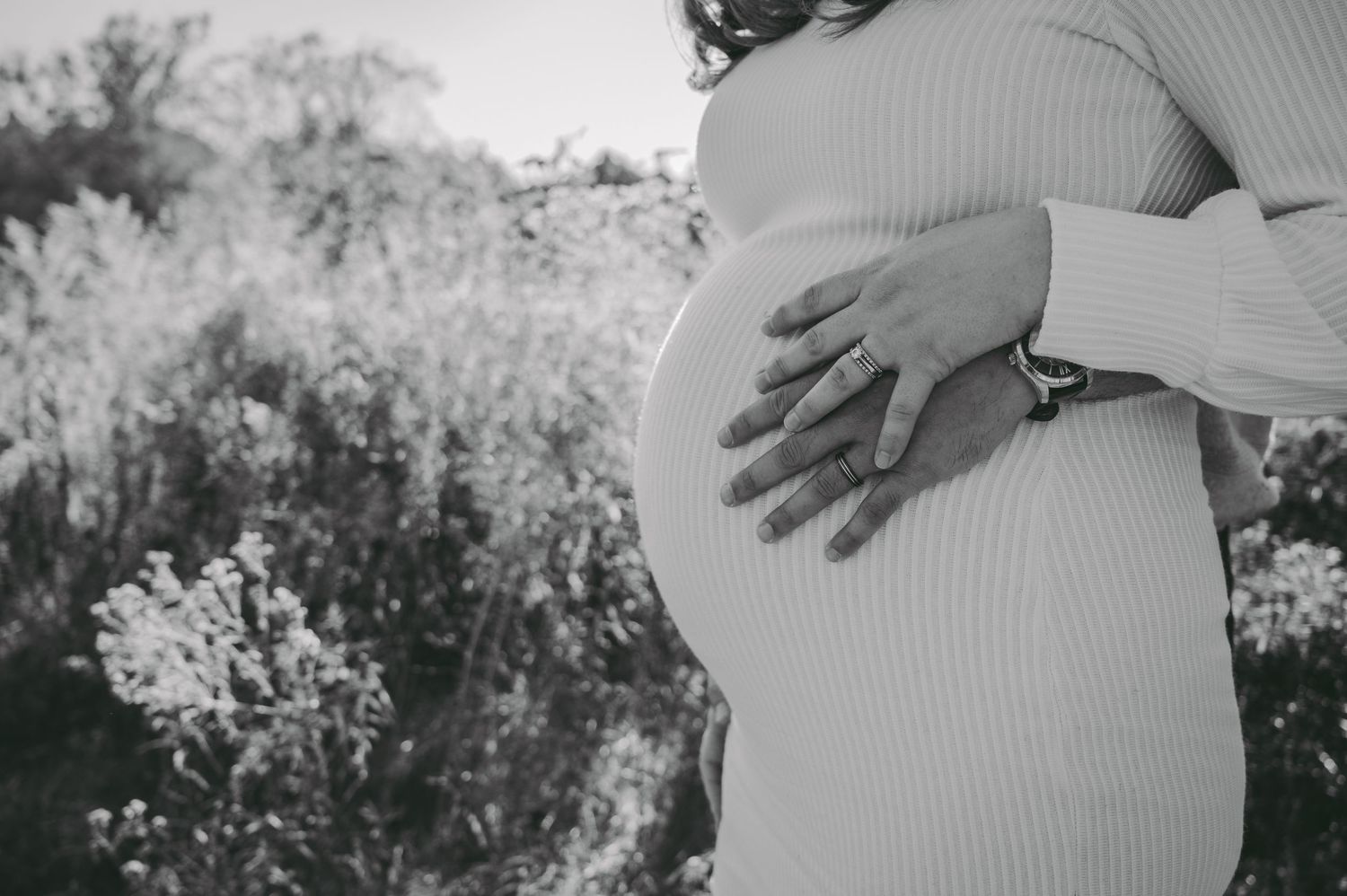 Close-up of hands cradling a pregnant belly in a ribbed white sweater.
