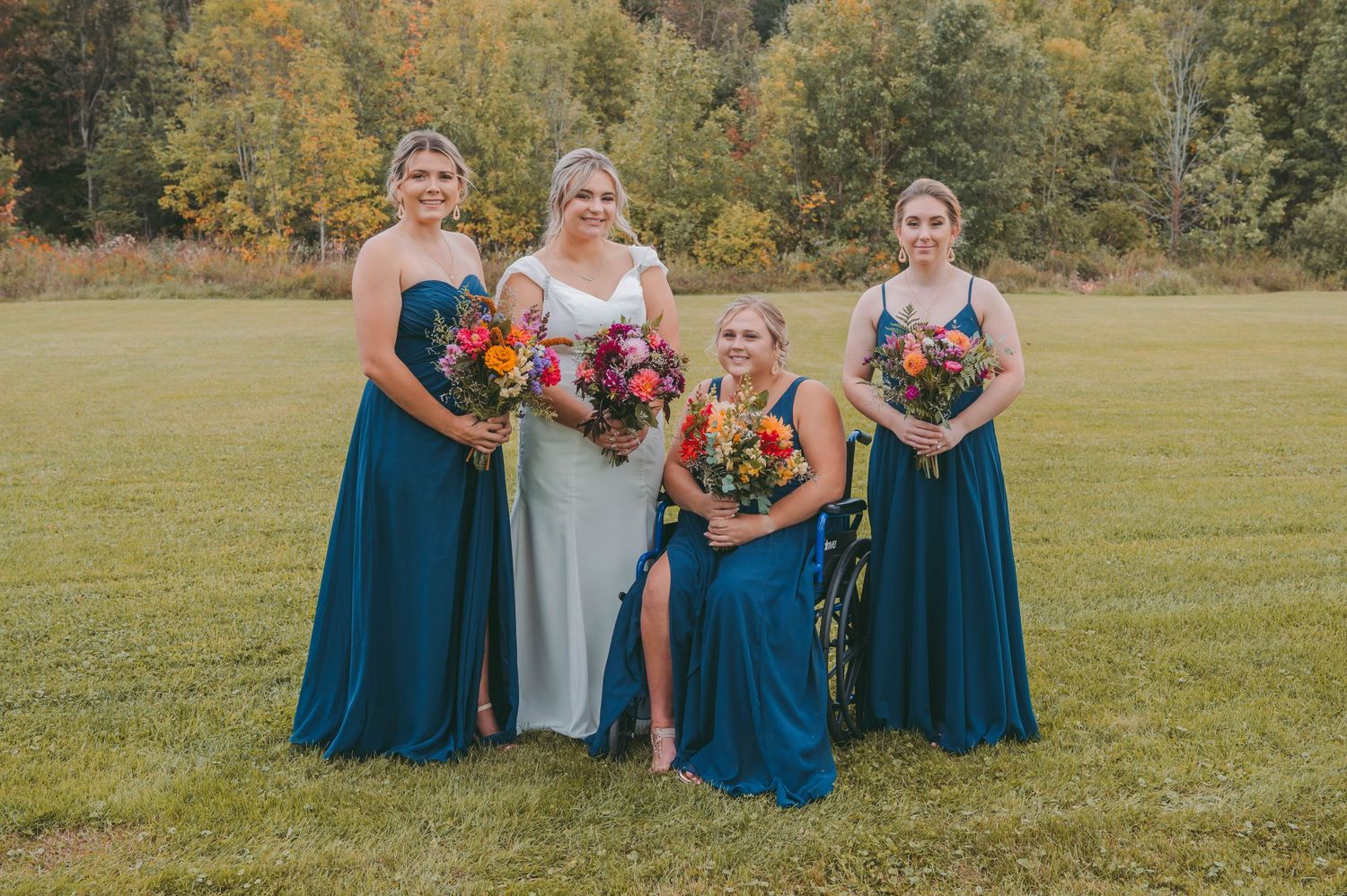 Wedding party in navy blue dresses poses with colorful bouquets during outdoor autumn ceremony.