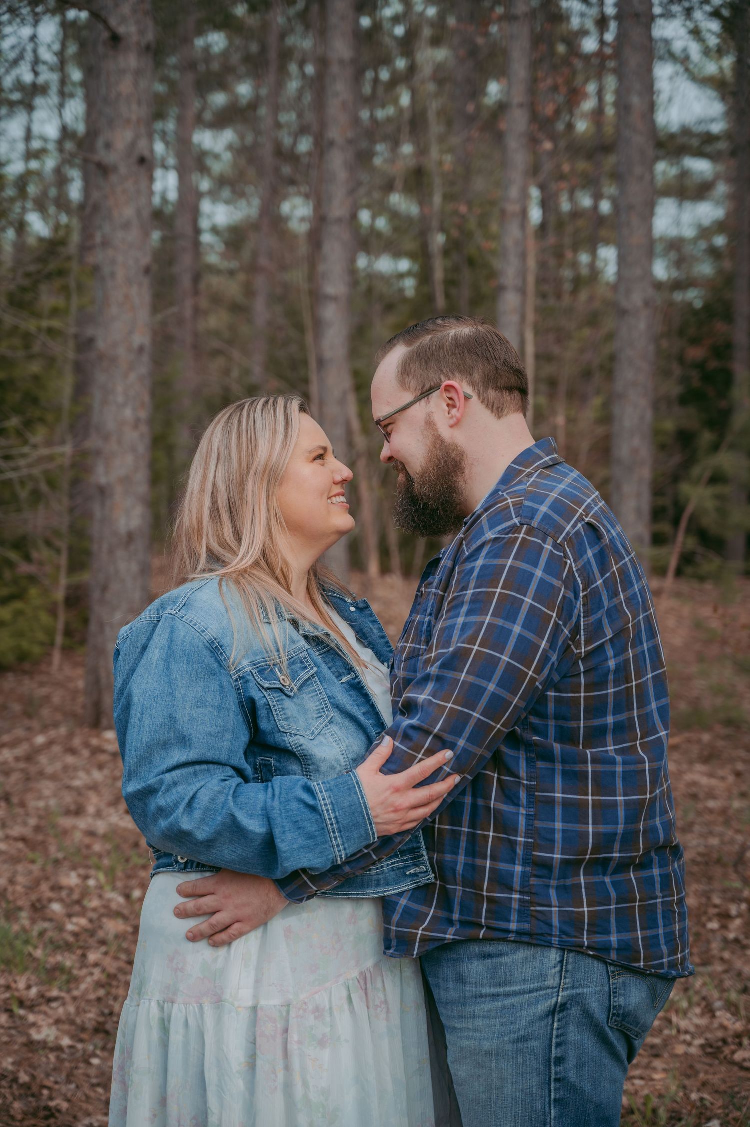 Casual forest engagement photo showing couple sharing a laugh in denim and plaid.