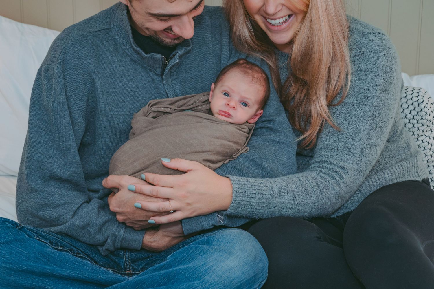 A cozy family moment on a gray couch with a newborn baby wrapped in soft blankets.