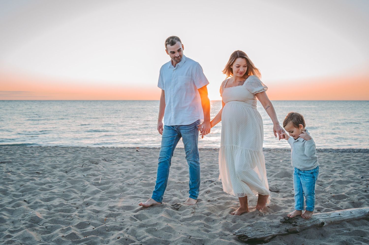 A family holds hands while walking together on a sandy beach during sunset against an orange sky background.