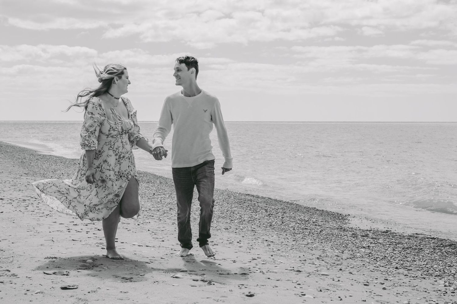 Monochrome capture of couple strolling along rocky shoreline with ocean view.