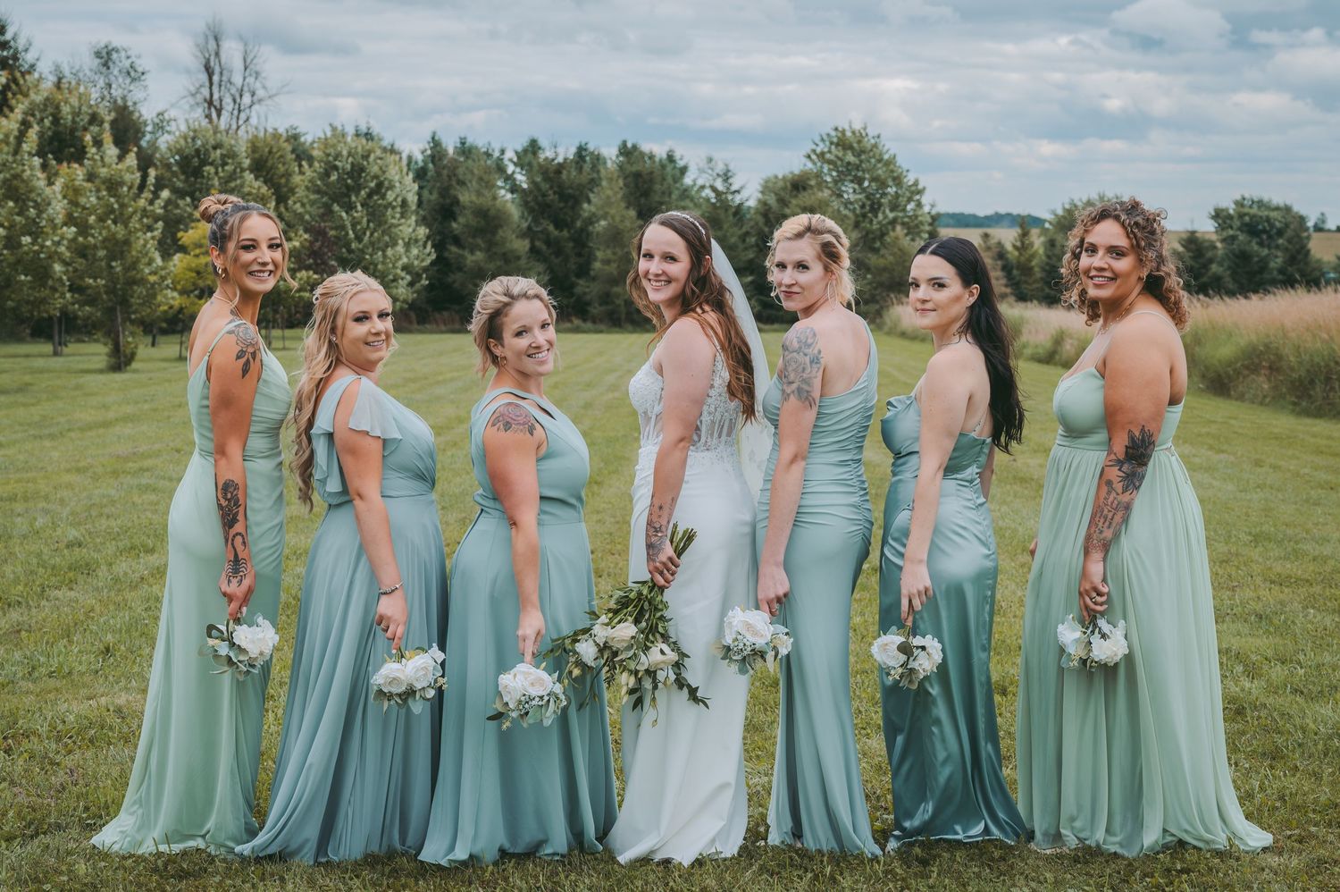 Bridesmaids in mint green dresses pose together outdoors holding bouquets.