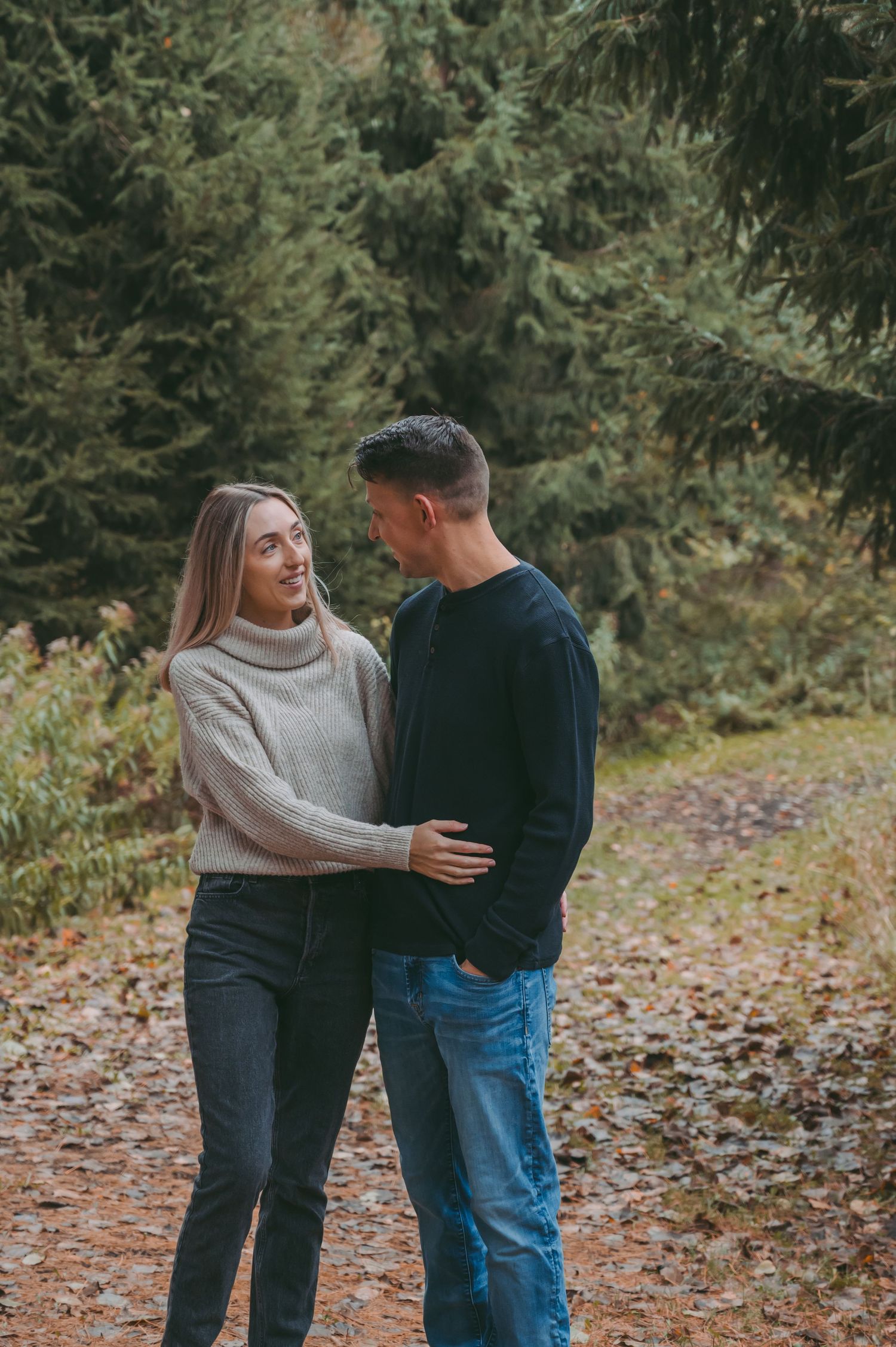 Young couple in sweaters sharing a romantic moment on a leaf-covered forest path.