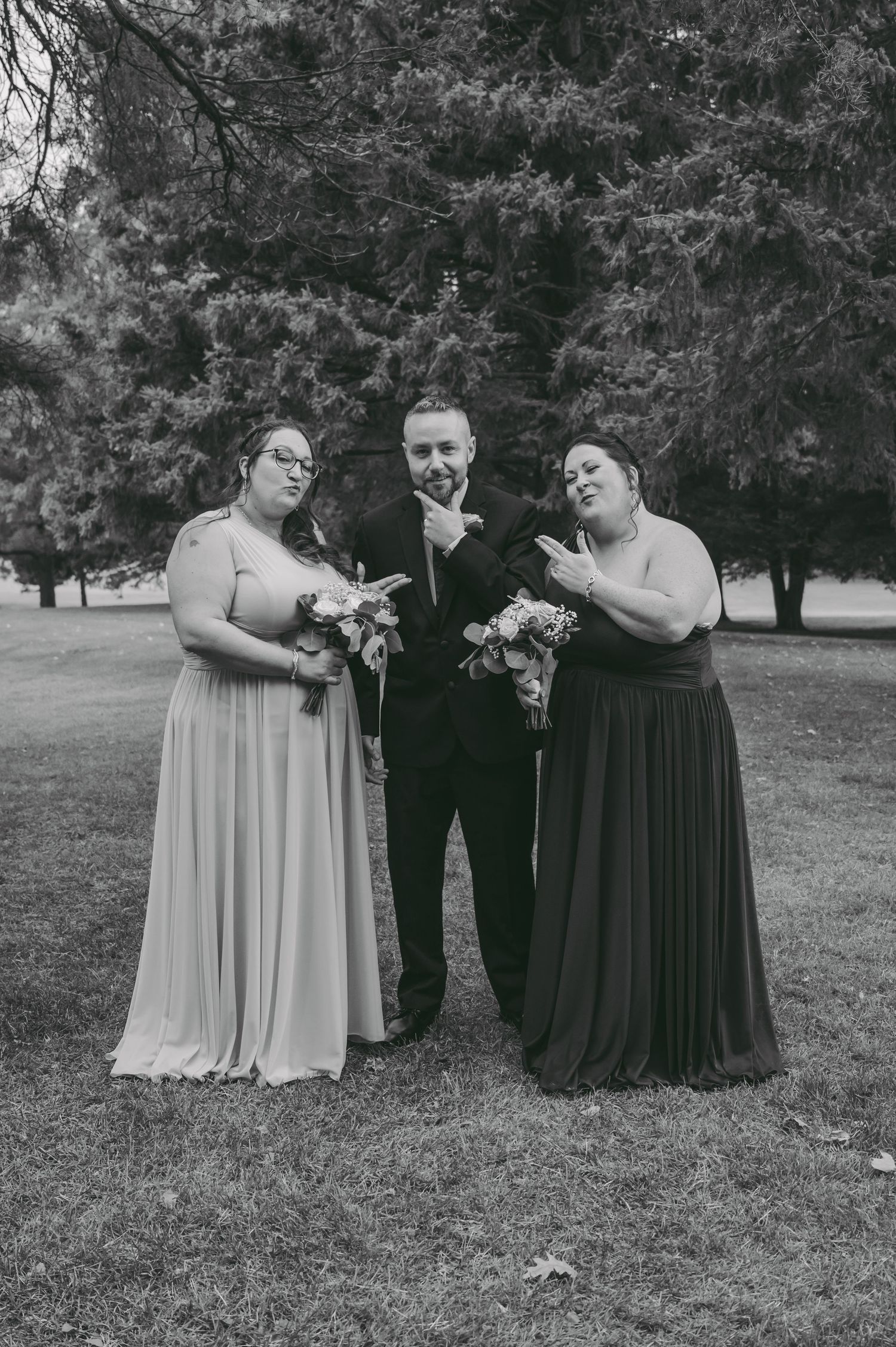 Wedding party members pose for black and white portrait under trees.