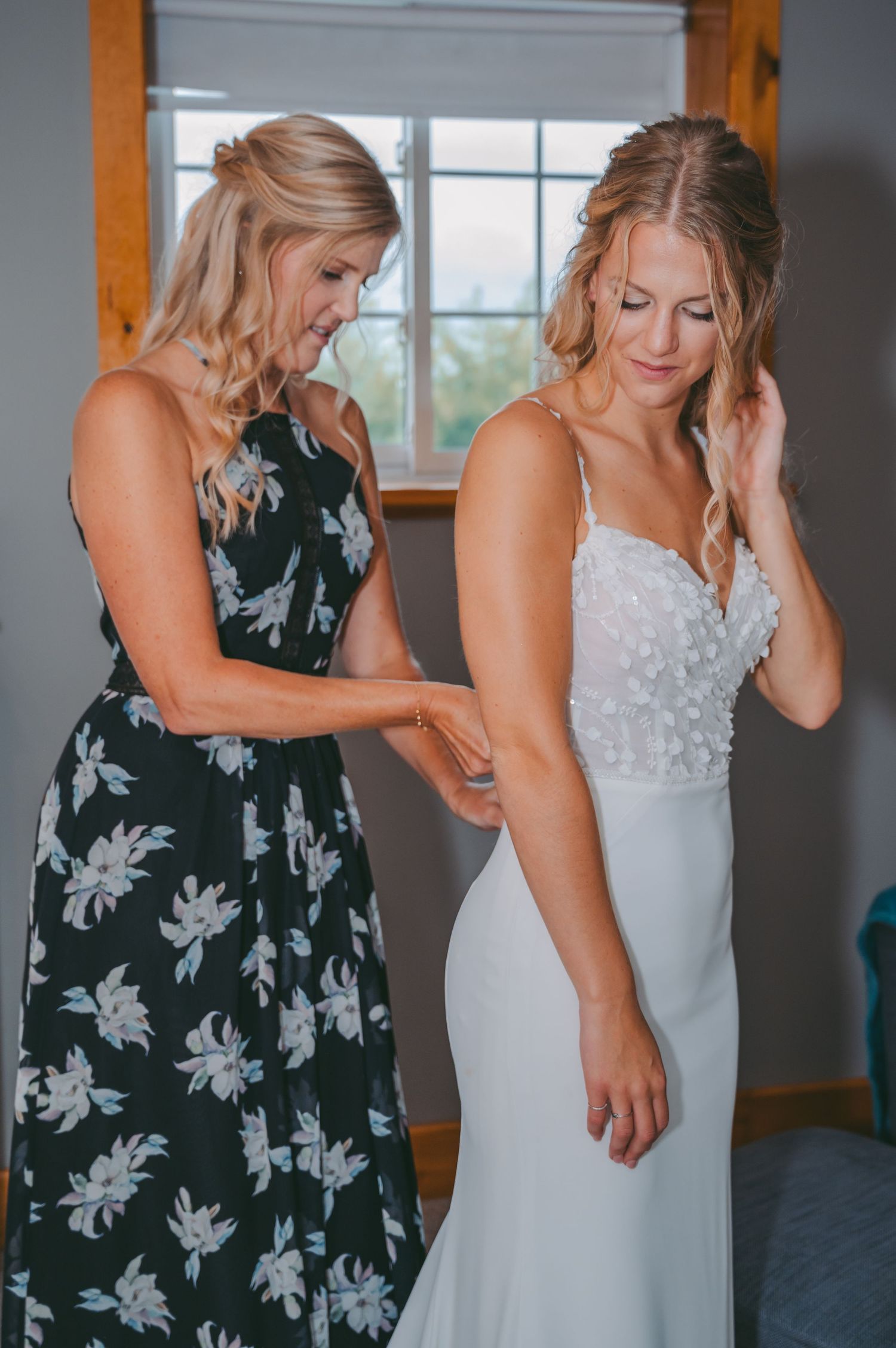 Two women in wedding attire sharing an emotional moment during preparation.