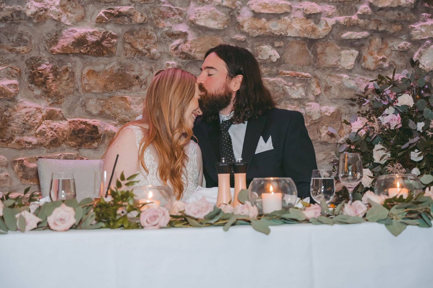 A romantic moment between newlyweds at their decorated sweetheart table with candles and flowers.