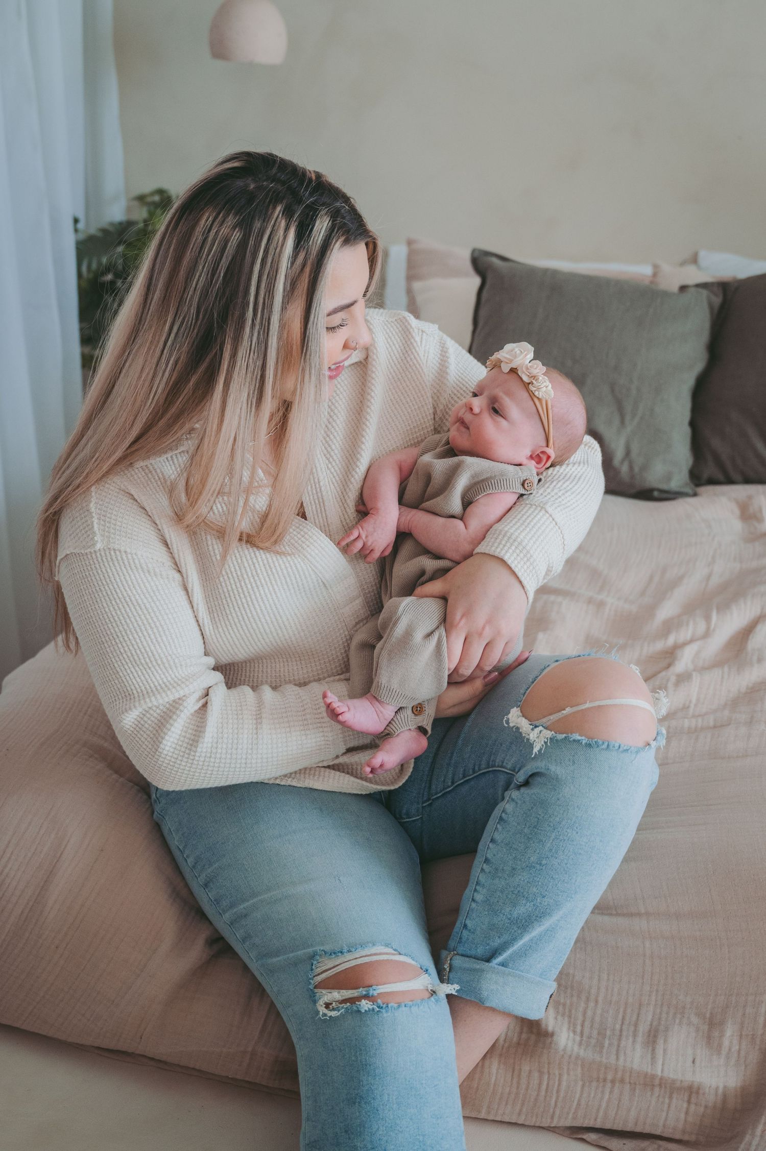 A tender moment between parent and infant sitting on a couch in casual attire of cream sweater and distressed jeans.