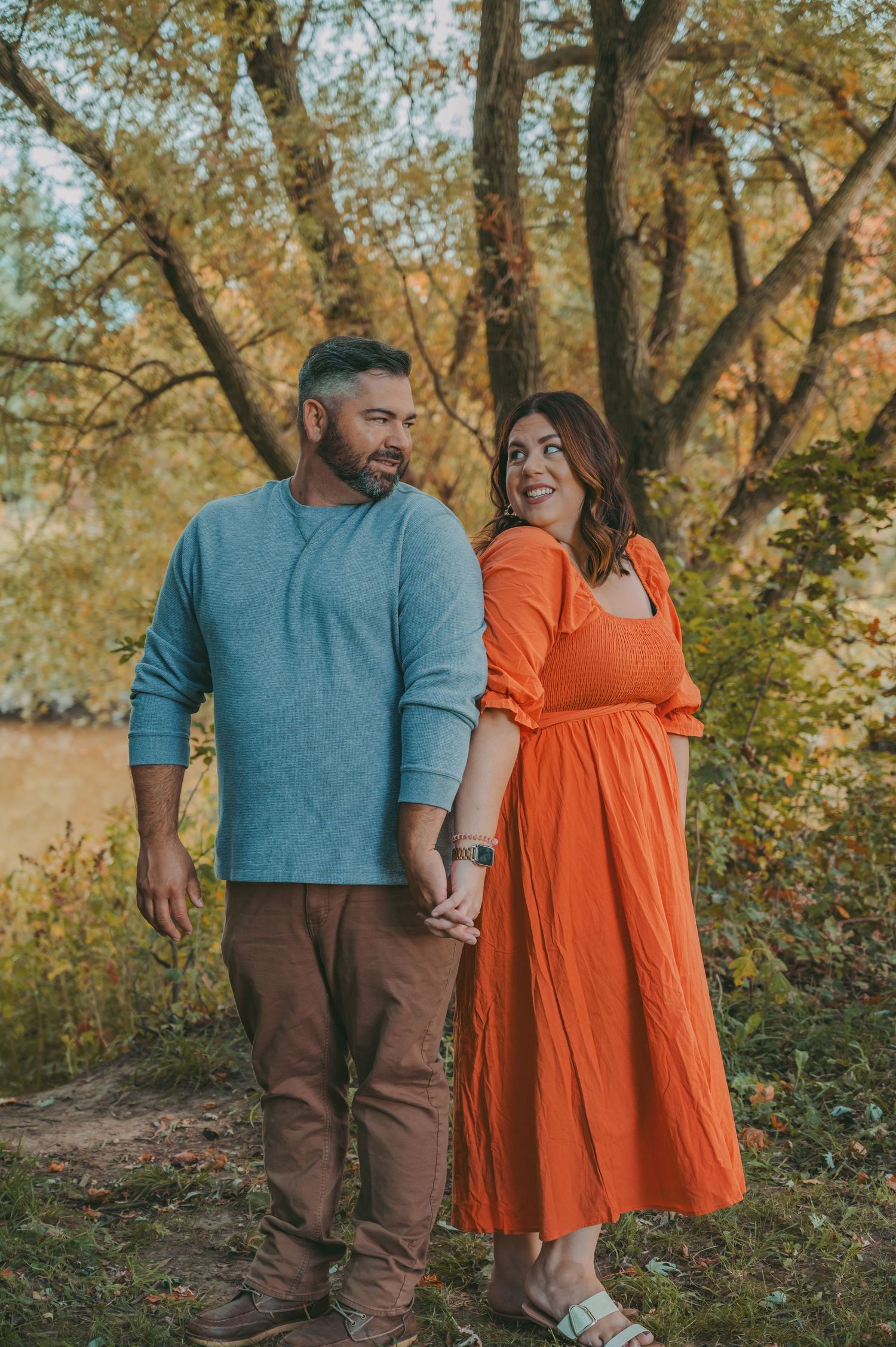 A couple holds hands while walking through a golden autumn landscape.