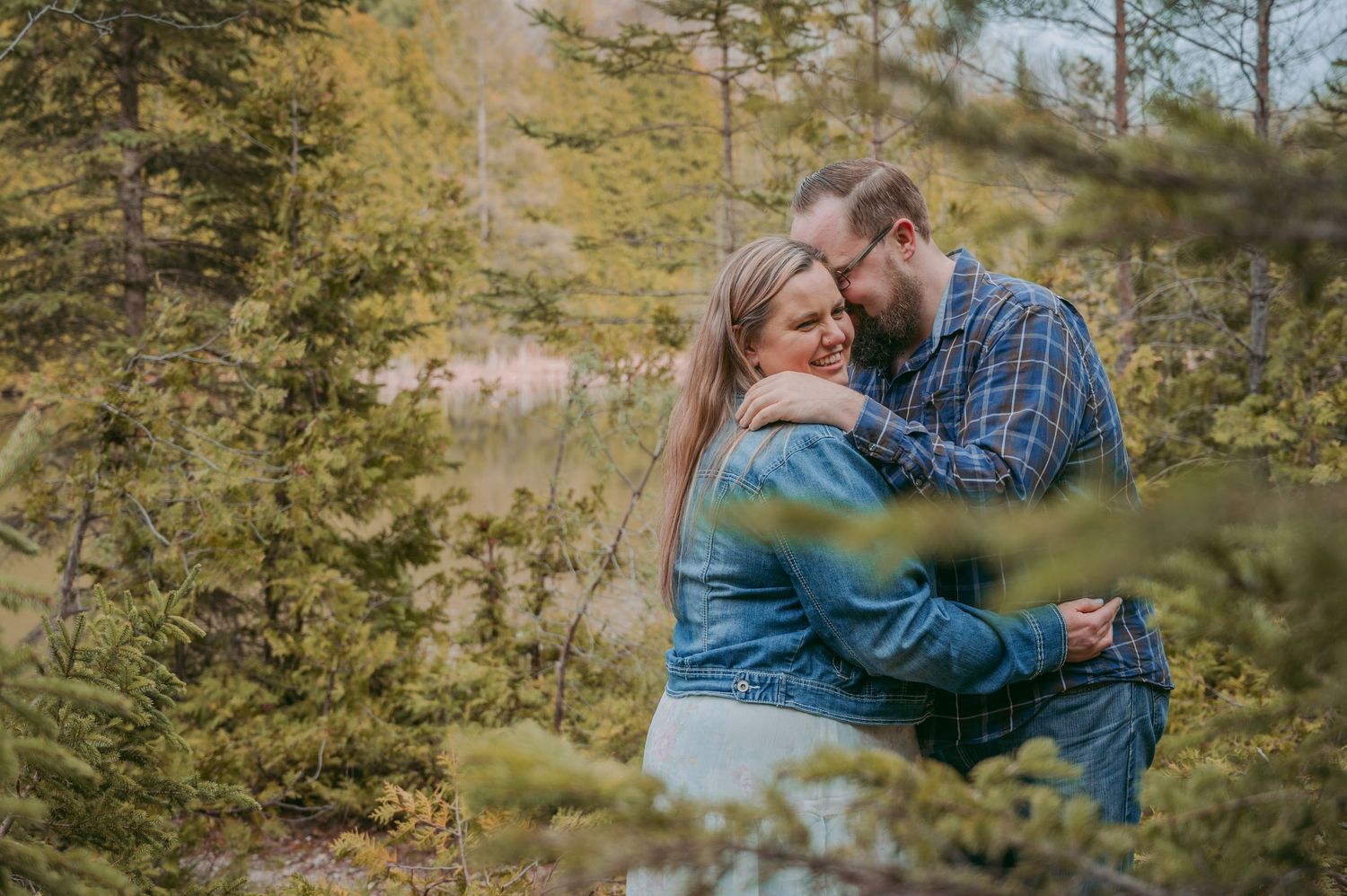 Intimate moment between couple captured through pine branches in natural lighting.