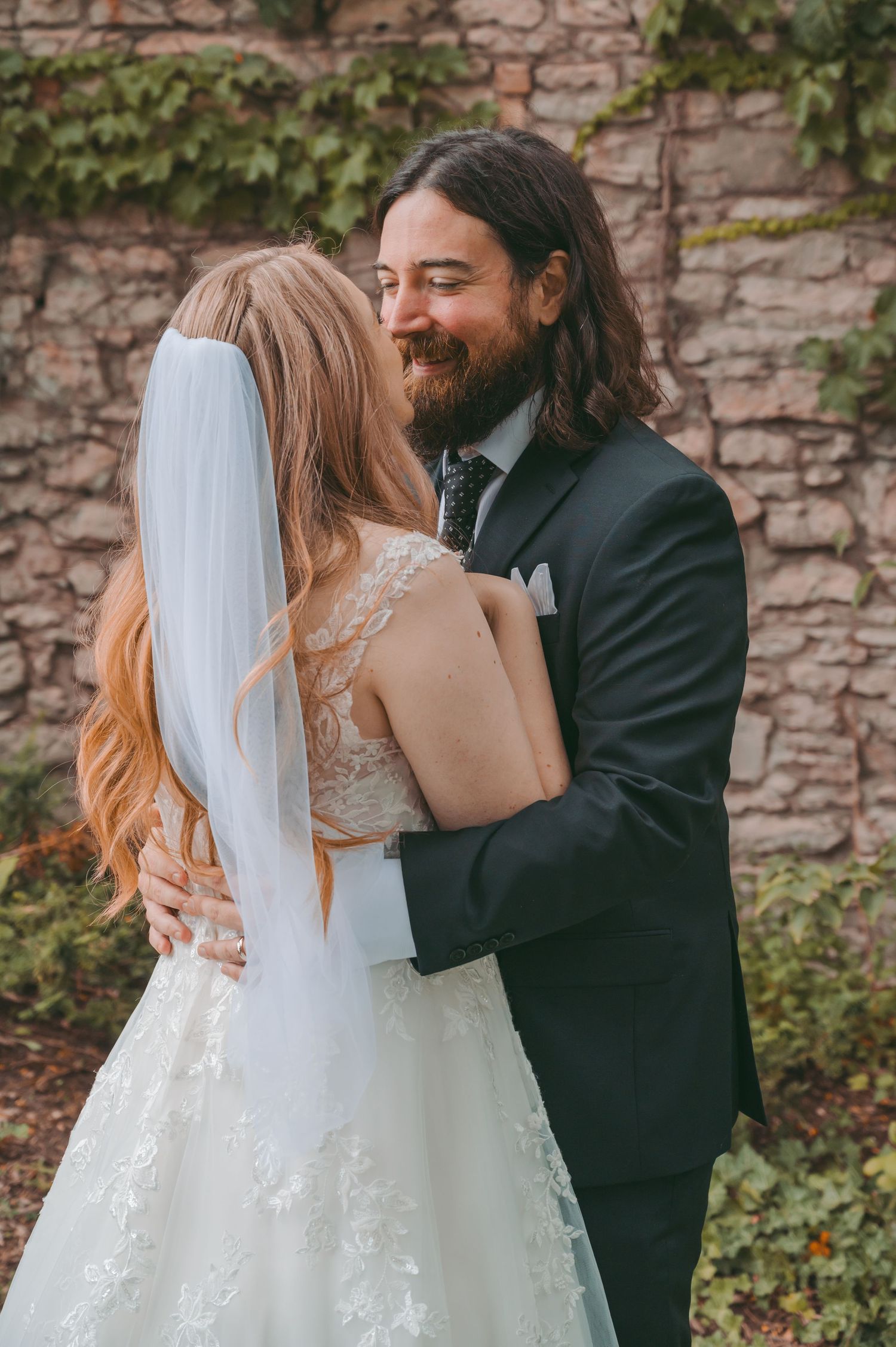 Tender wedding moments captured against a rustic stone wall with climbing ivy.