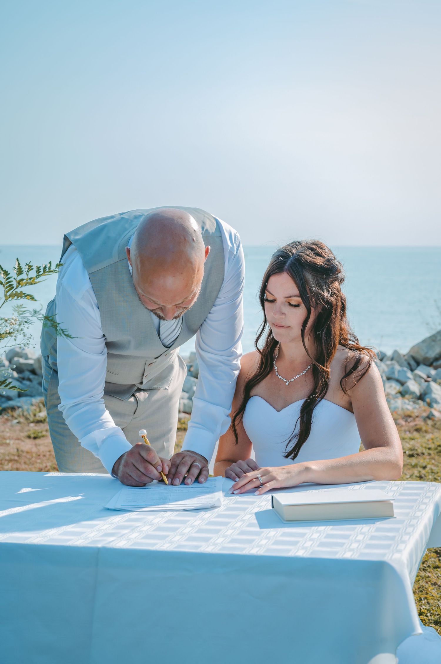Couple signing wedding documents at an outdoor ceremony overlooking the ocean.