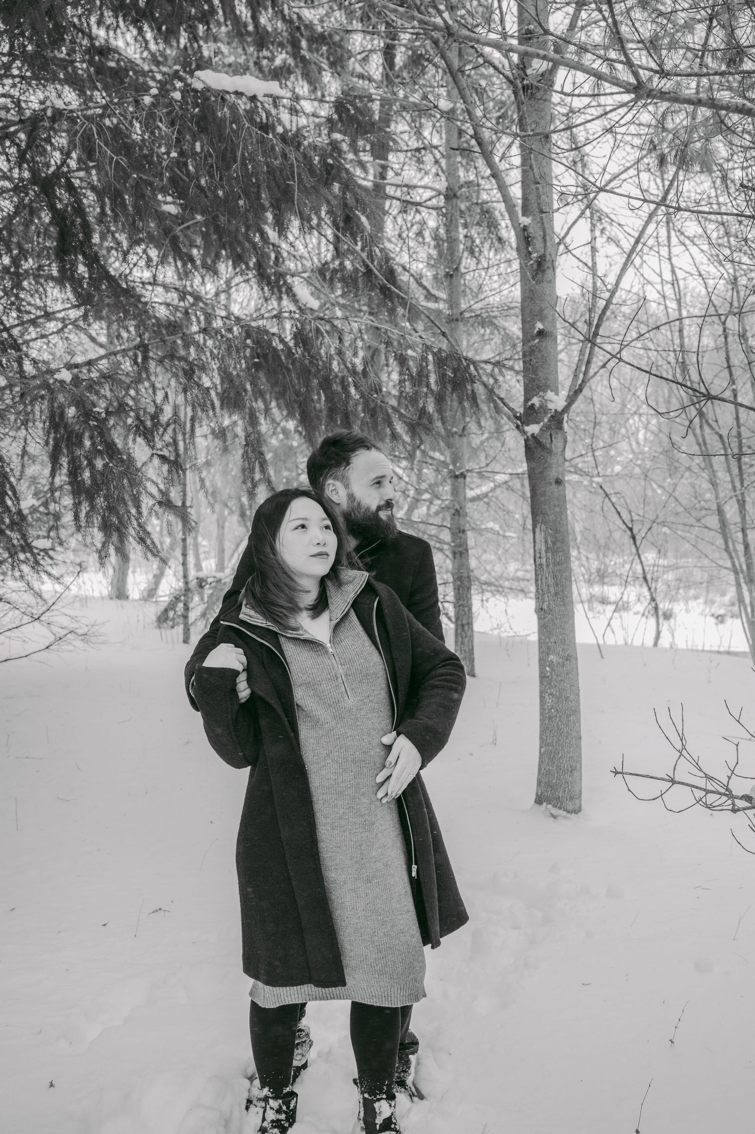 Winter photoshoot in a snowy forest with evergreen trees and figures in dark coats.