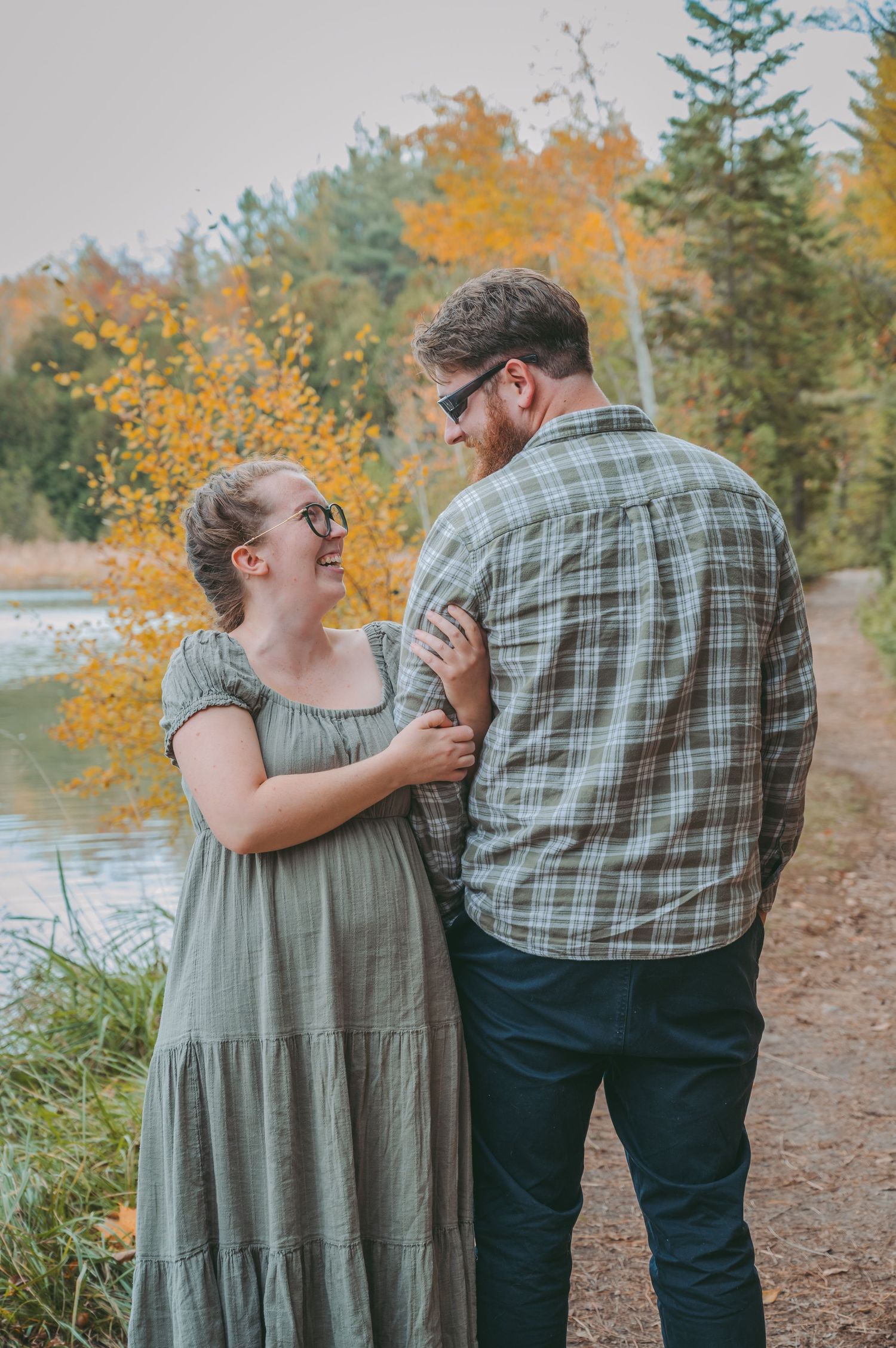 Couple shares intimate moment on nature trail with autumn foliage in background.