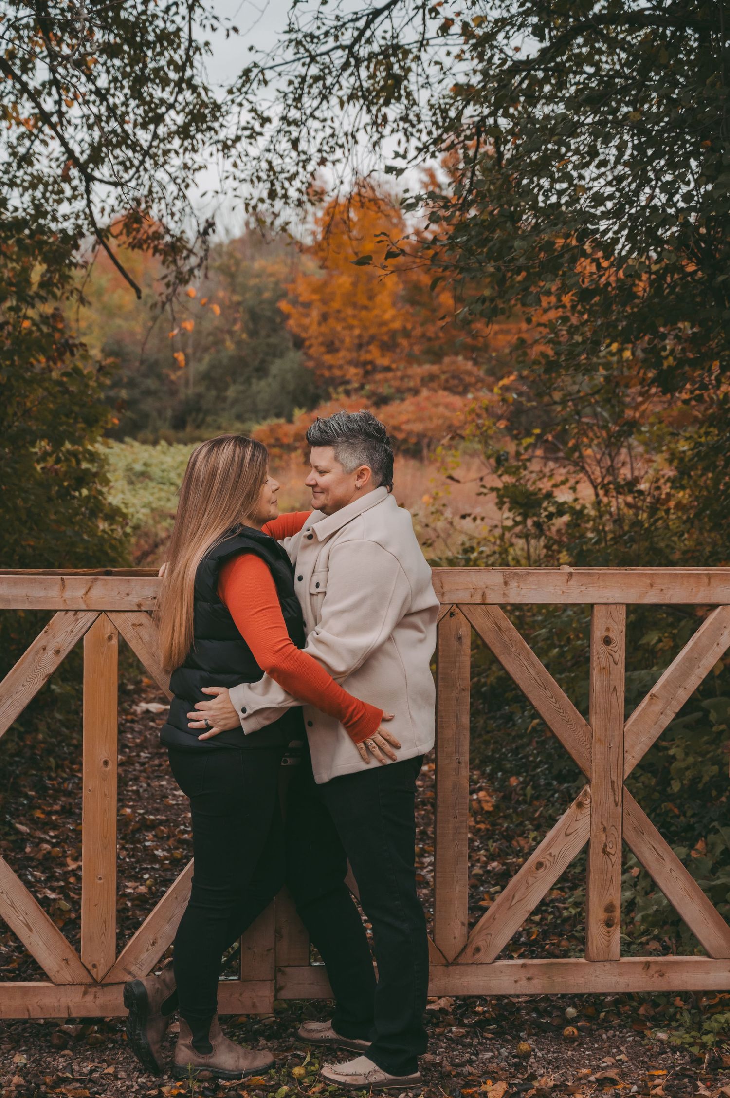A romantic autumn moment against a wooden fence with orange fall foliage in the background.