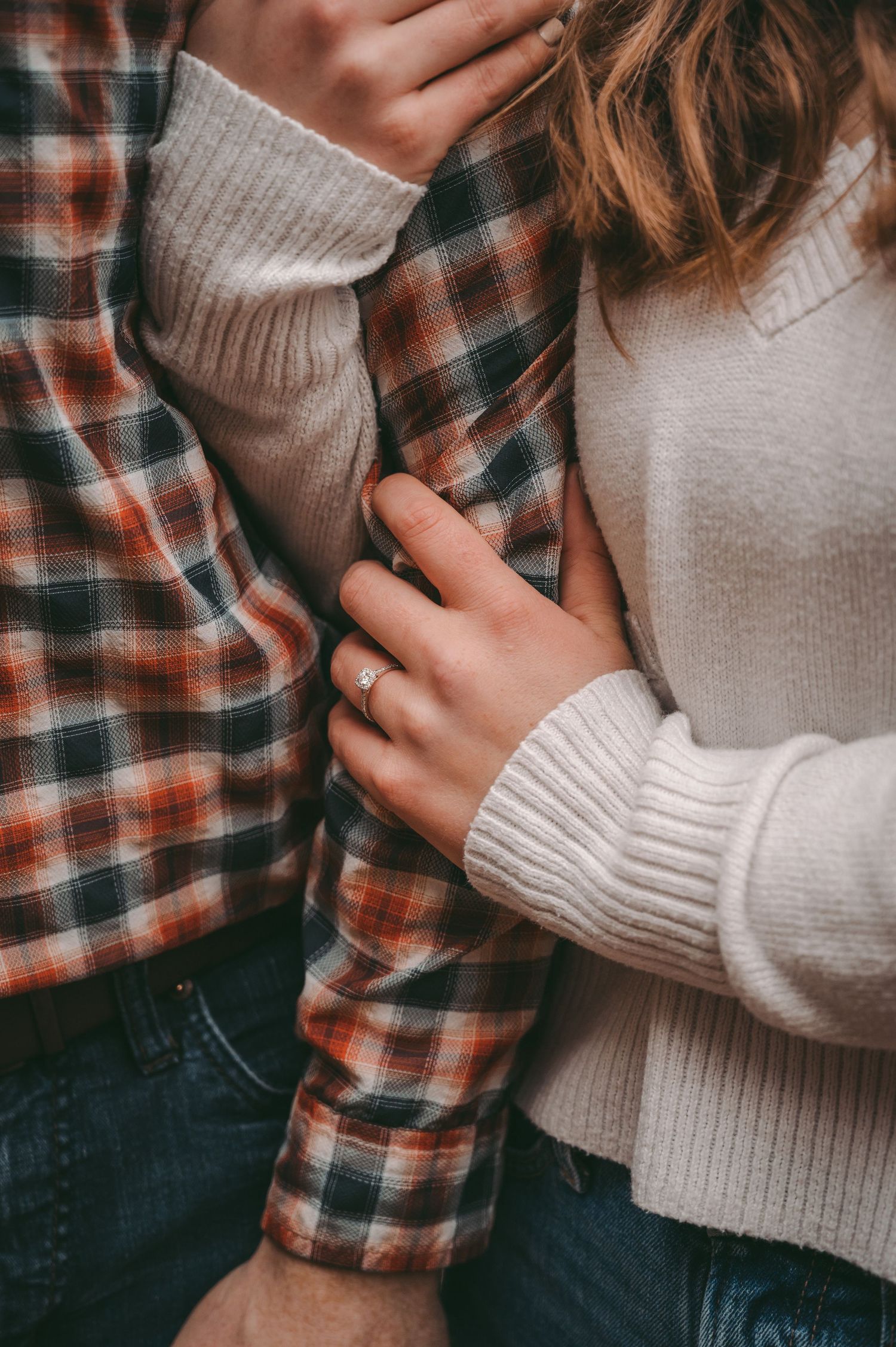 Close-up of hands in cozy sweaters with a plaid shirt showing an engagement ring.