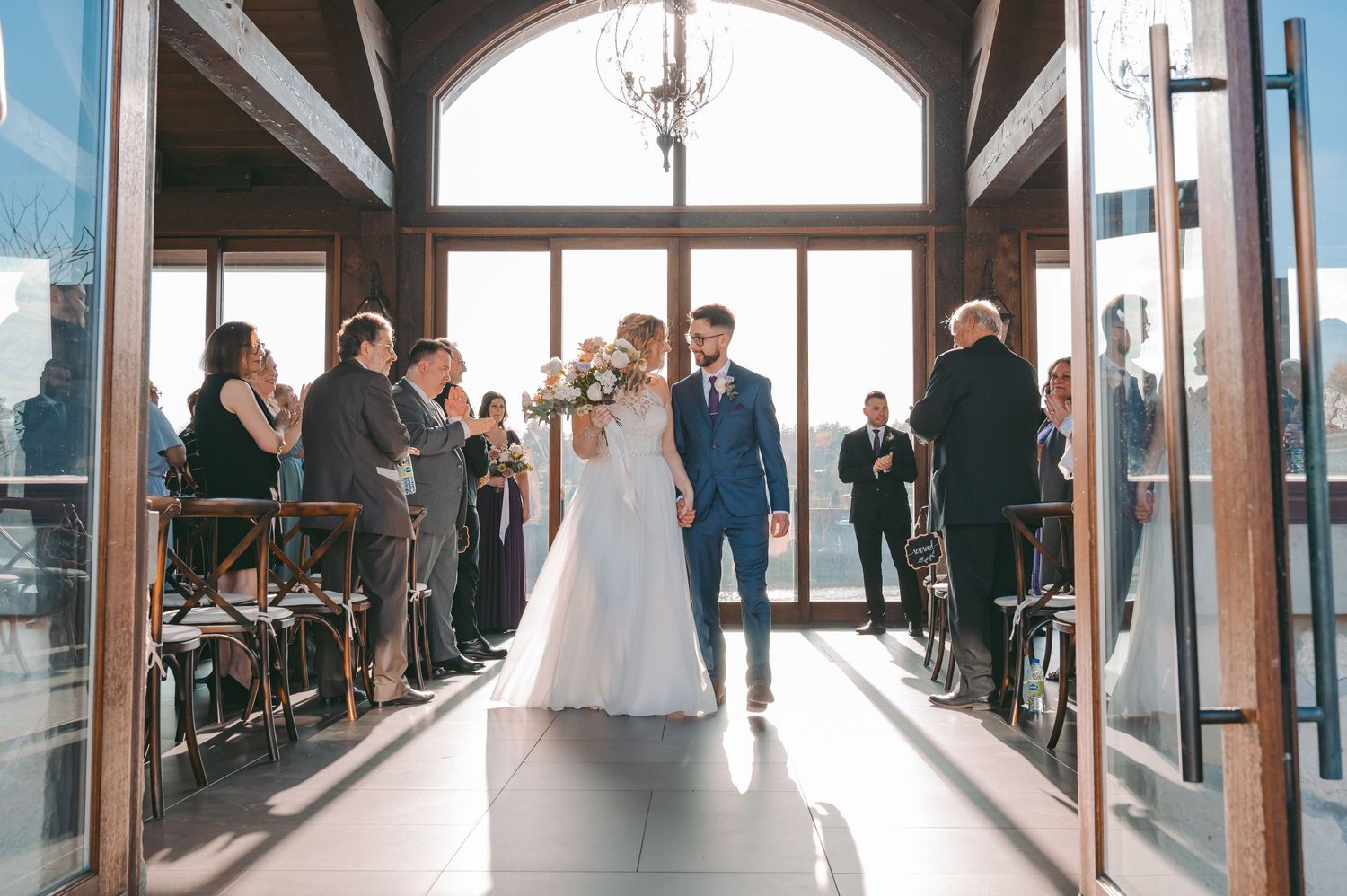 Wedding ceremony exit with guests lined up in sunlit Cambridge Mill venue with large windows.