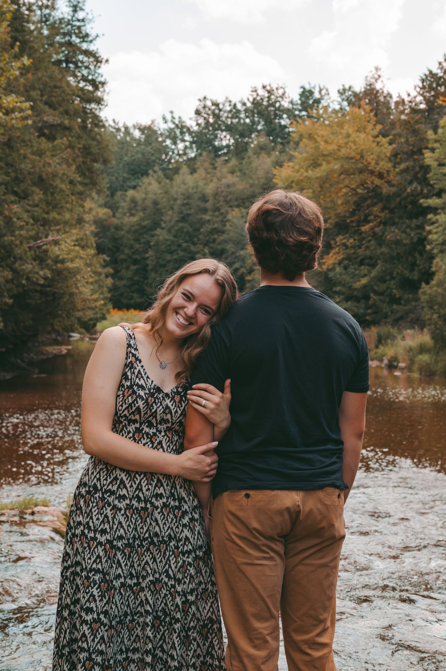 Candid moment of couple laughing together by riverside in autumn setting.