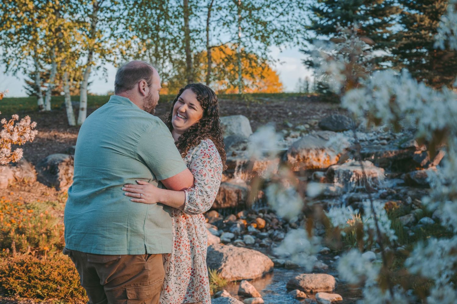A romantic sunset engagement photoshoot scene with autumn foliage and golden light filtering through.