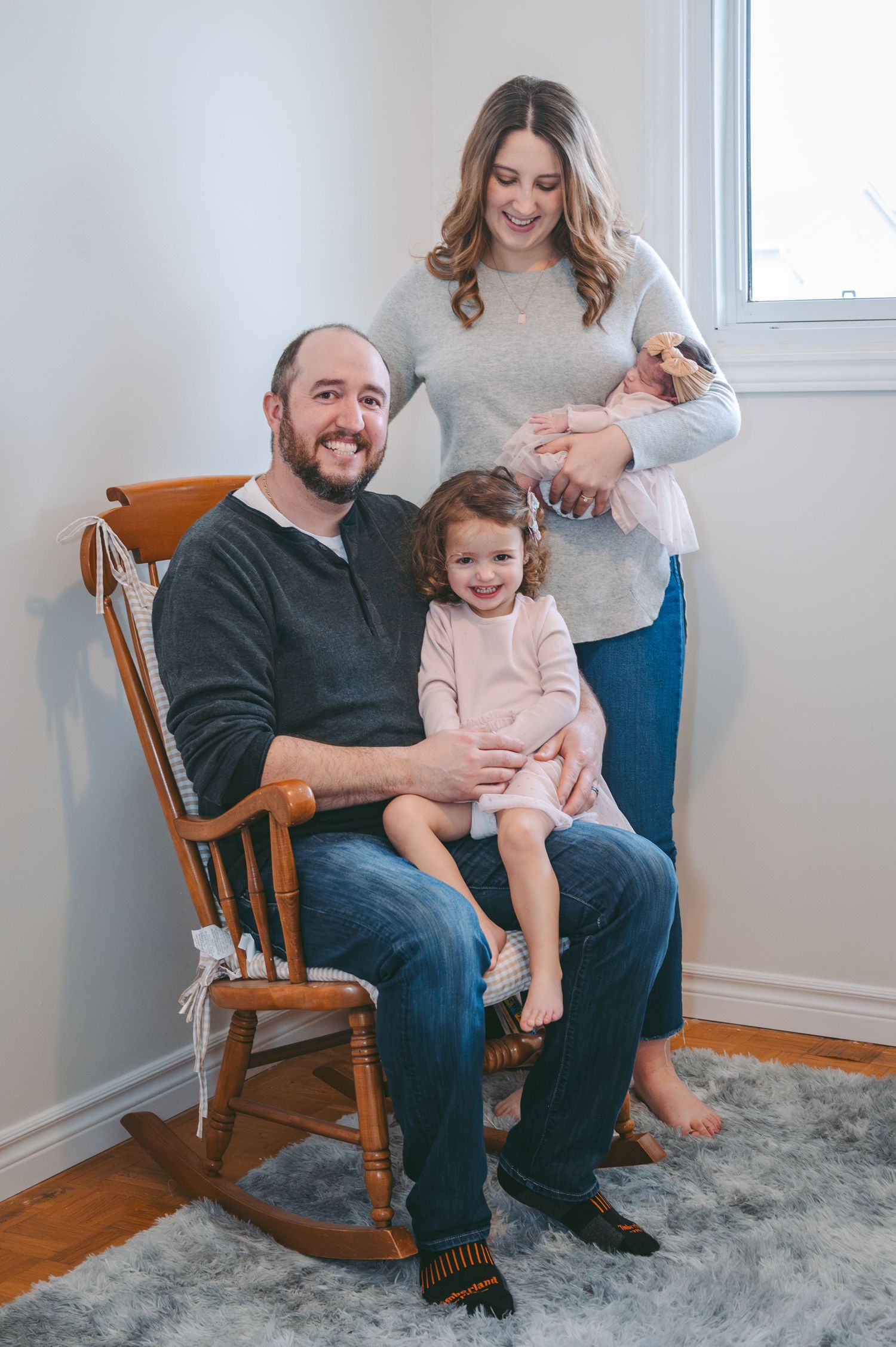 Family seated in a wooden rocking chair share joyful smiles in a bright room.