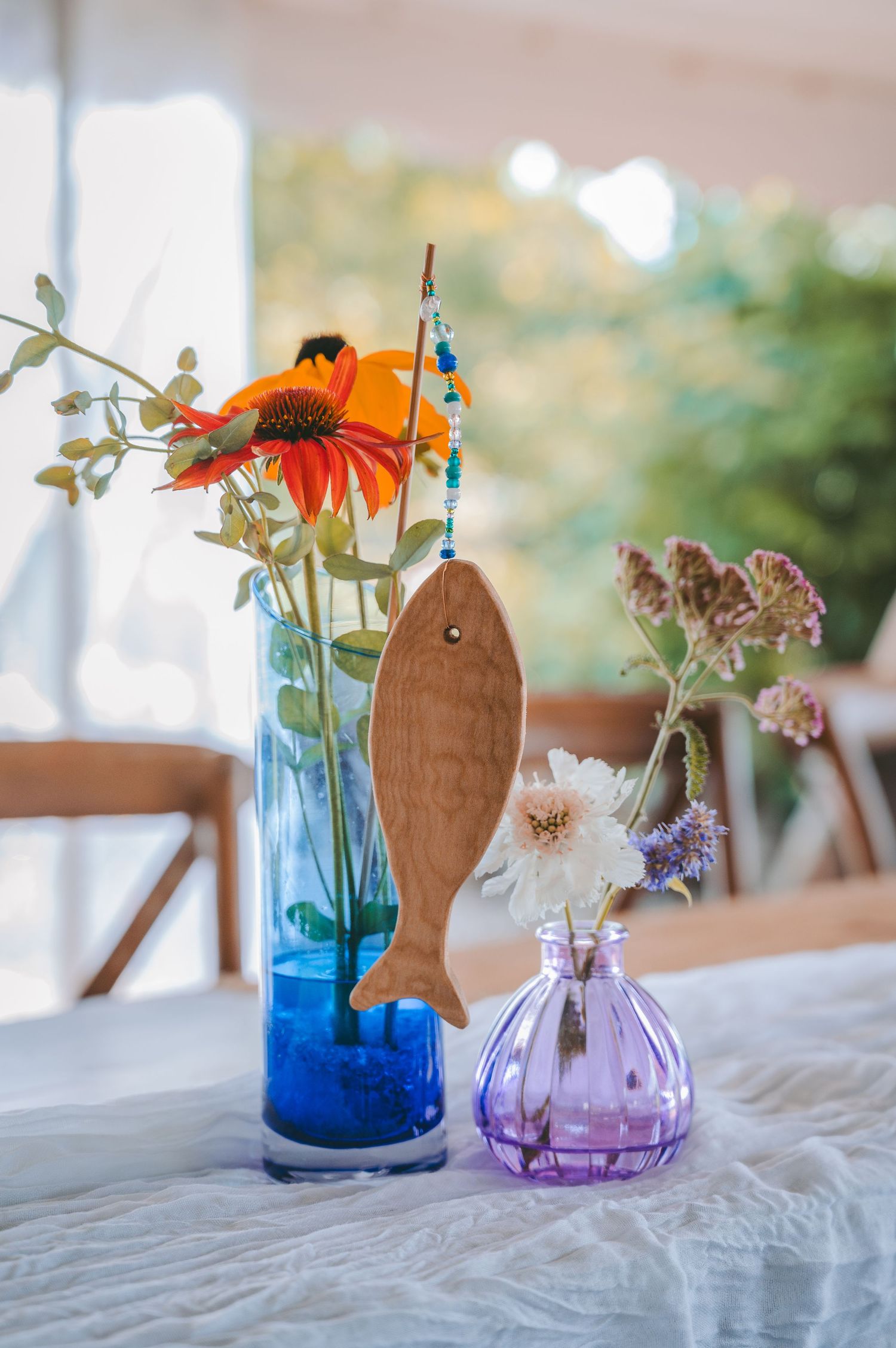 Colorful floral arrangement with orange coneflowers and wildflowers in blue and purple glass vases on a white tablecloth.