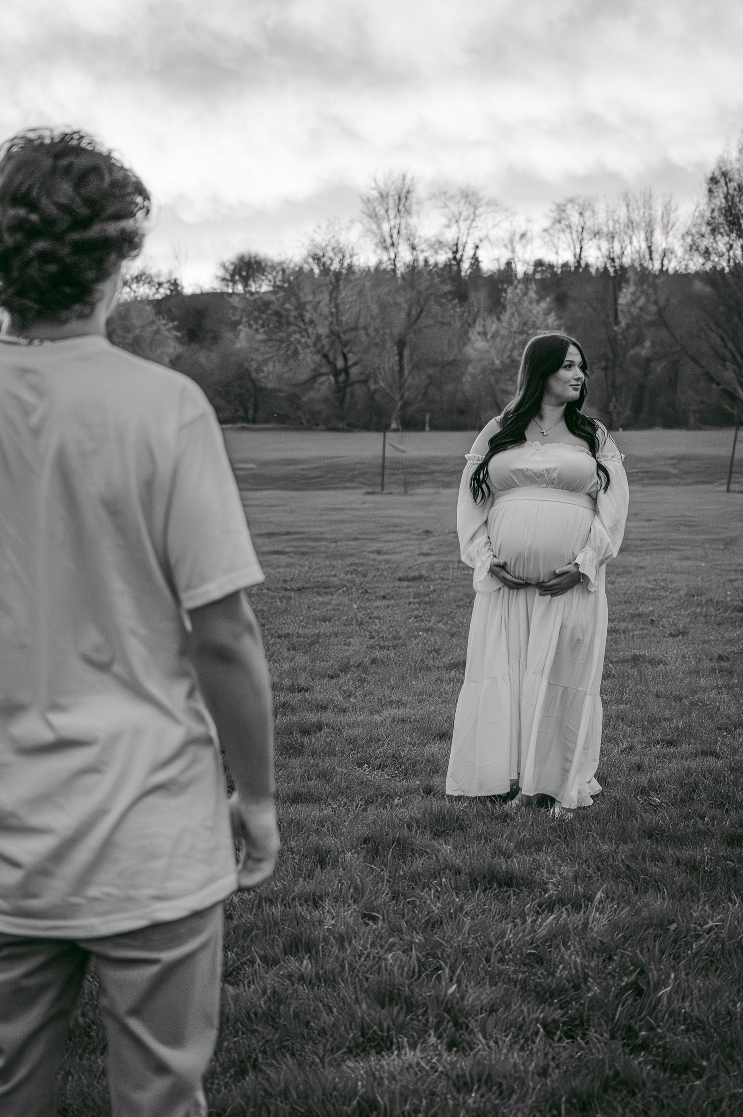 A black and white maternity photography session showing a couple in a serene outdoor setting.