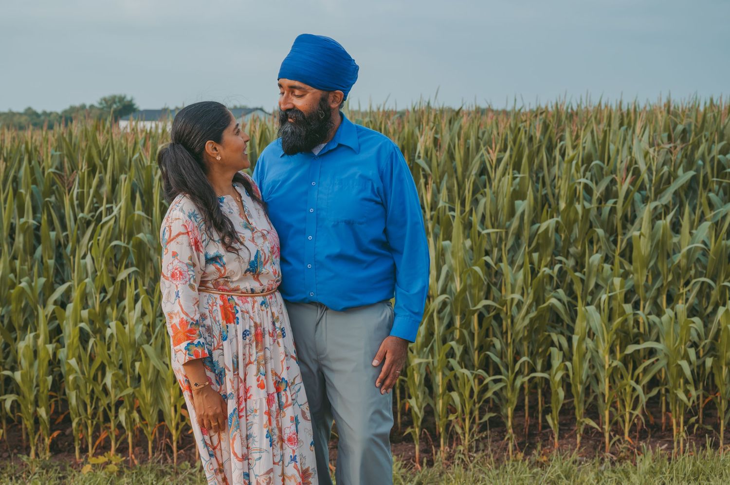 A couple walking together along a cornfield during golden hour.