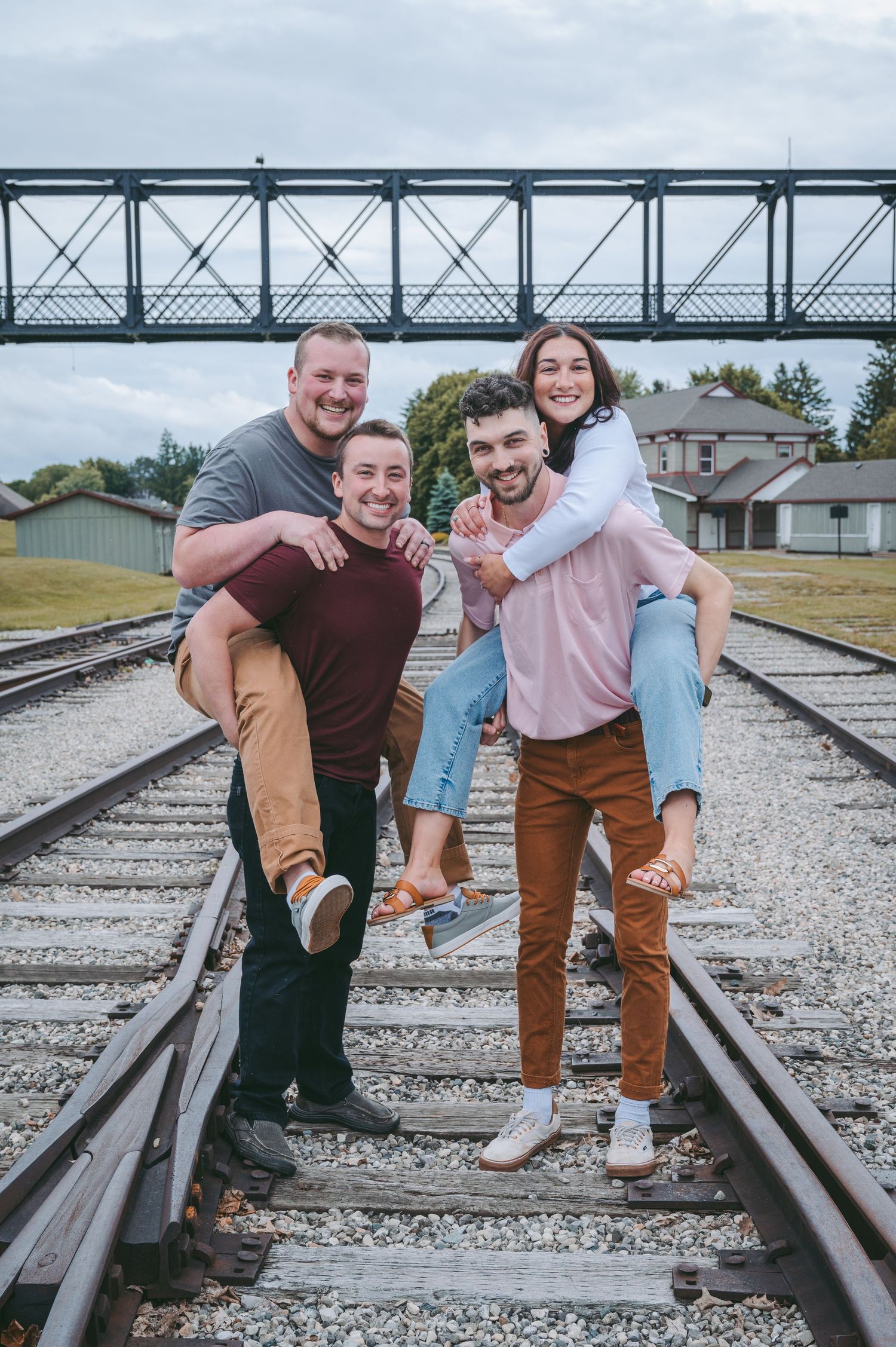 Friends share a fun piggyback moment on railroad tracks beneath a steel bridge.
