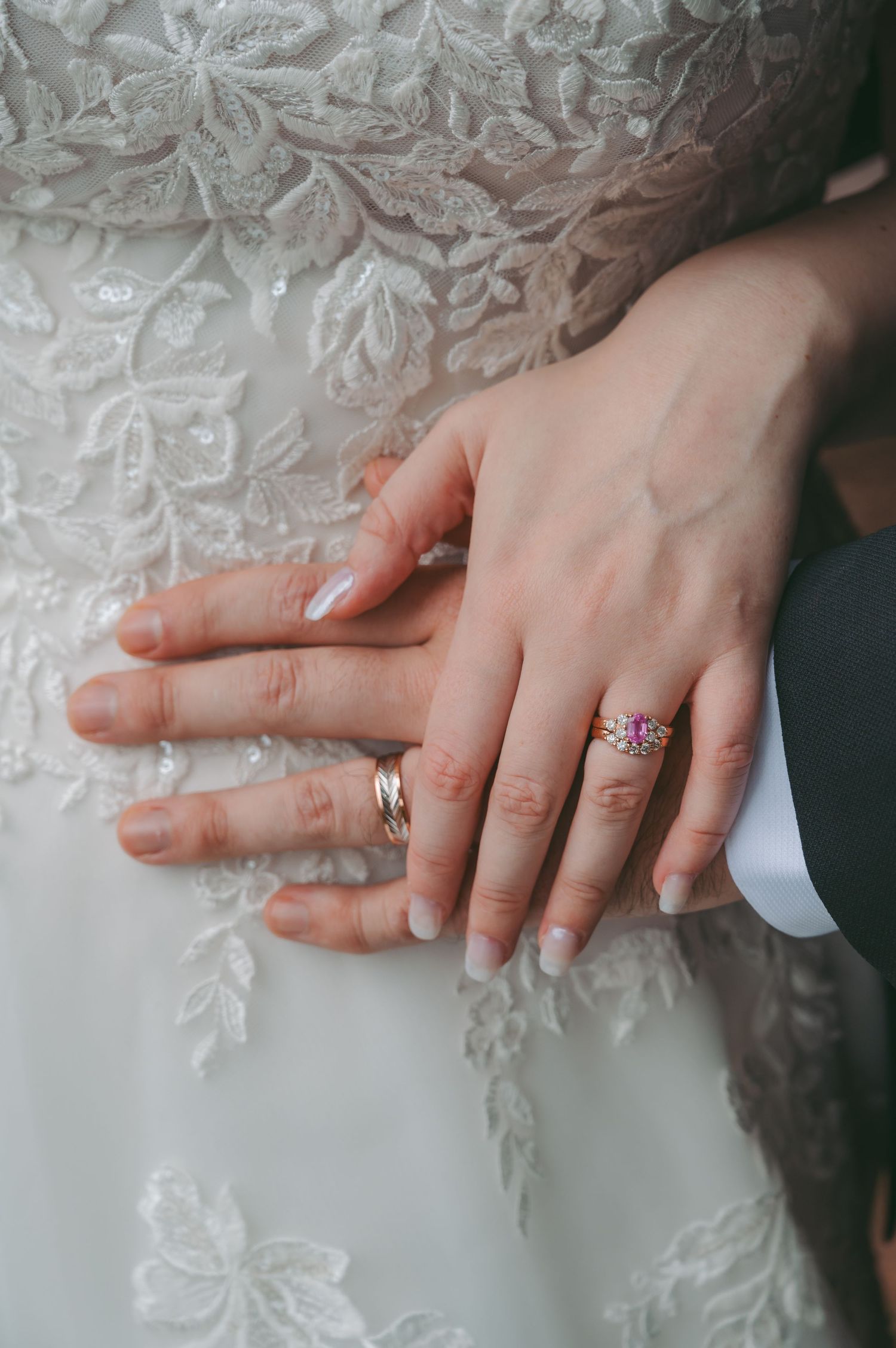 Close-up of wedding rings and hands against intricate lace dress detail.