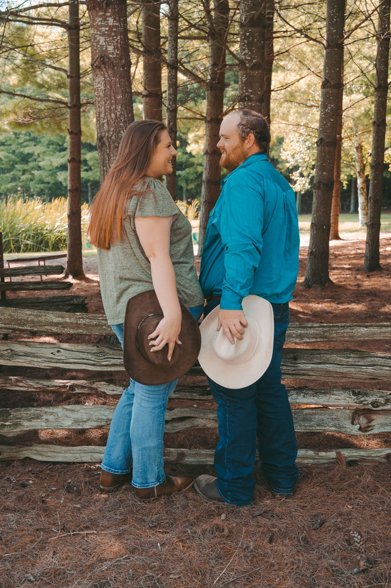 A romantic couple in western attire share an intimate moment among tall pine trees.