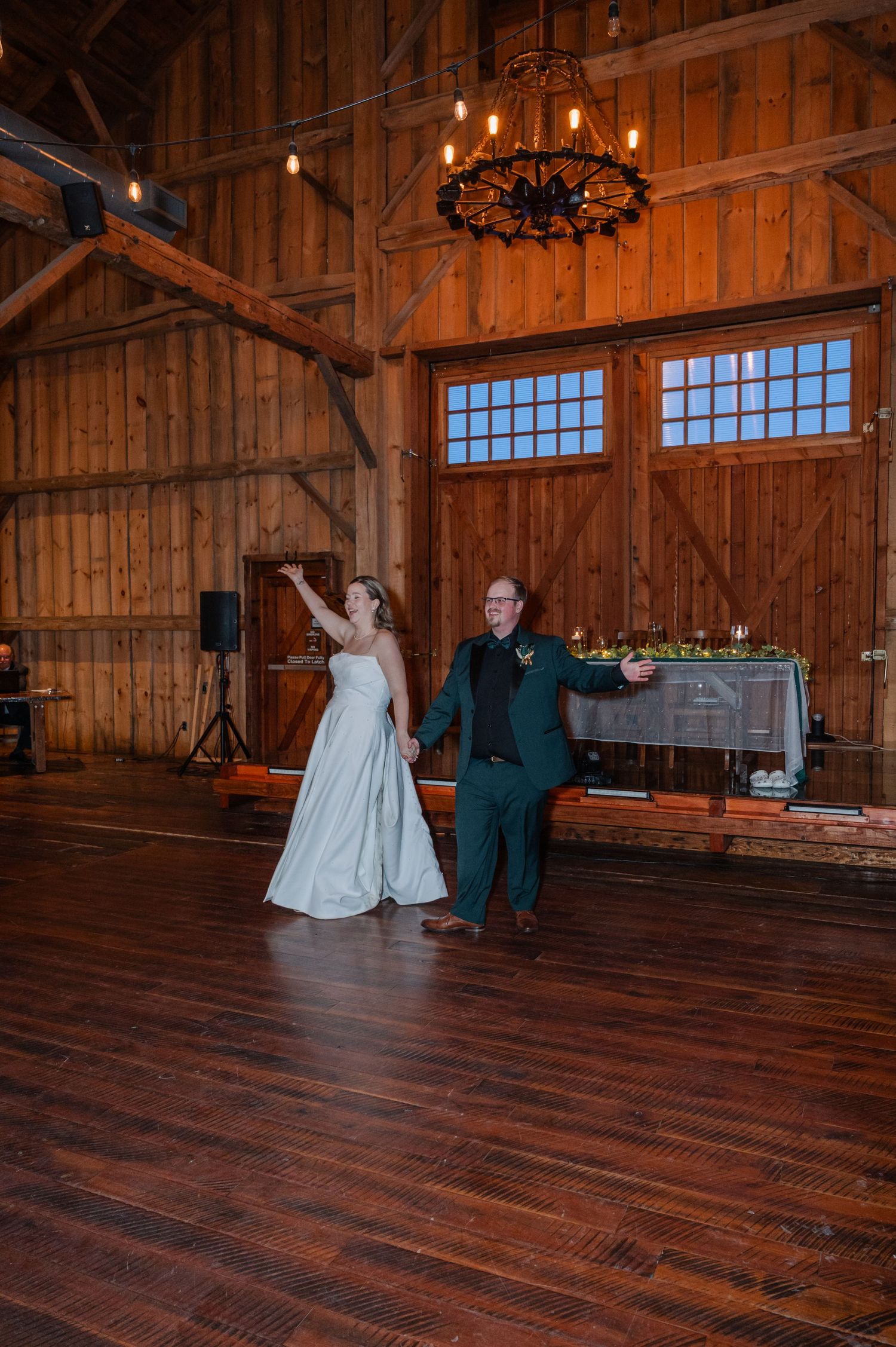 Bride and groom share their first dance in a rustic barn venue with wooden floors and chandelier.