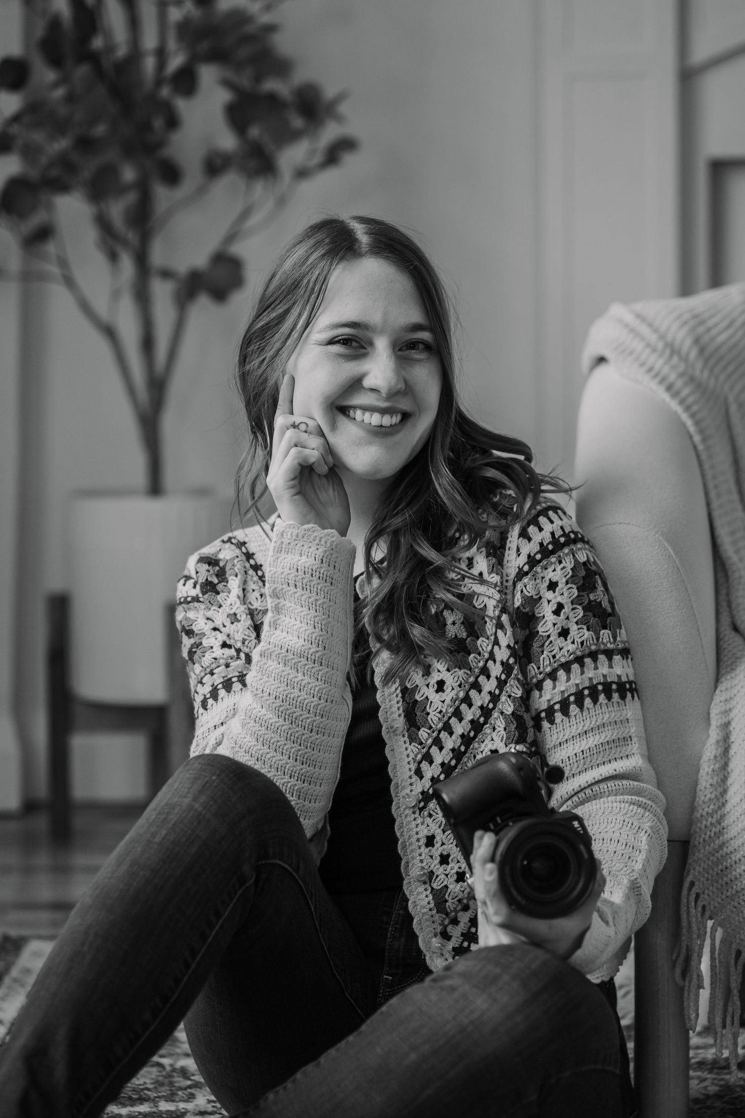 Black and white photo series of a photographer holding a camera while sitting and smiling in casual attire.