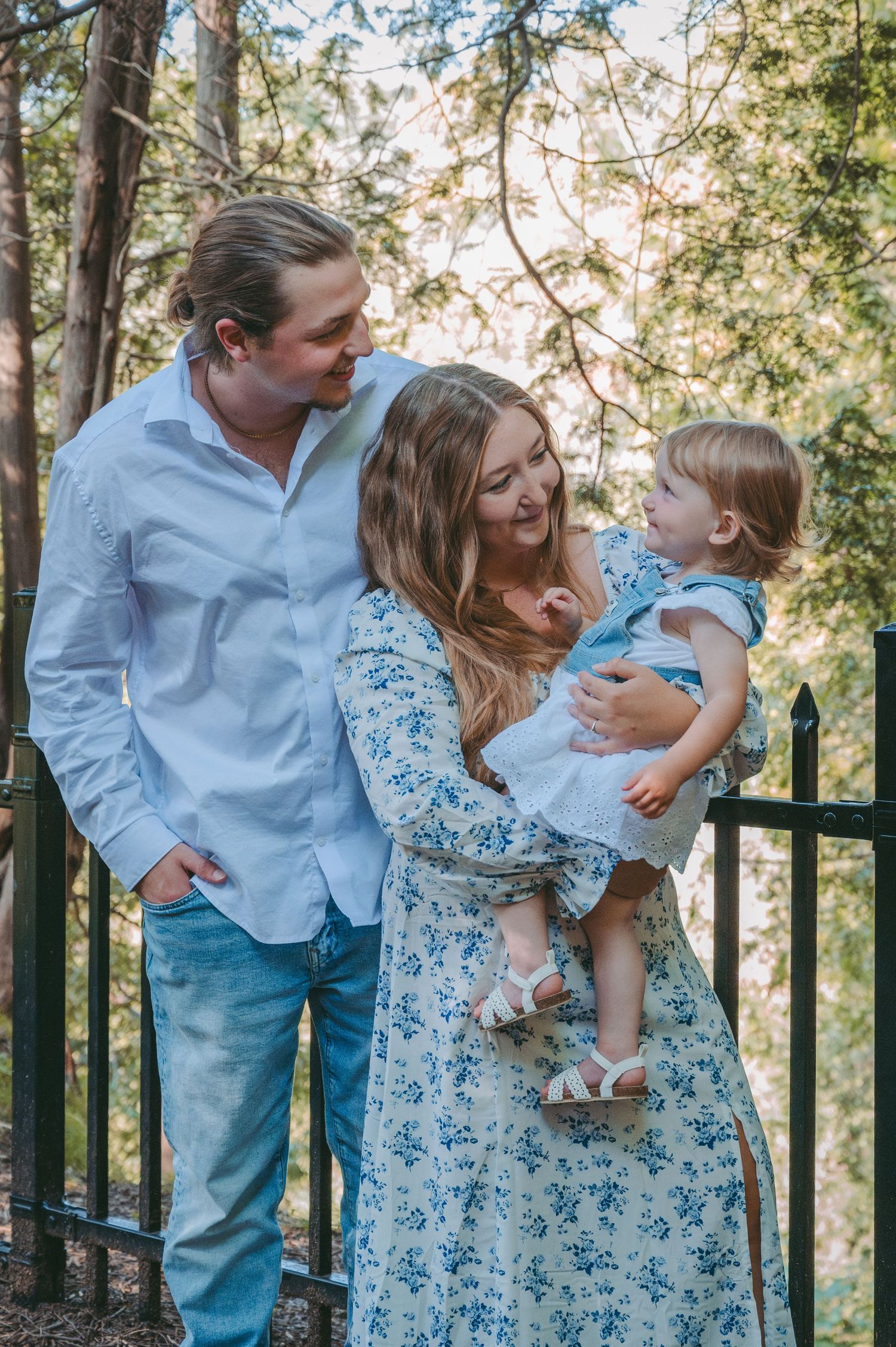 A family shares a joyful moment together against a wooded backdrop near a black iron fence.